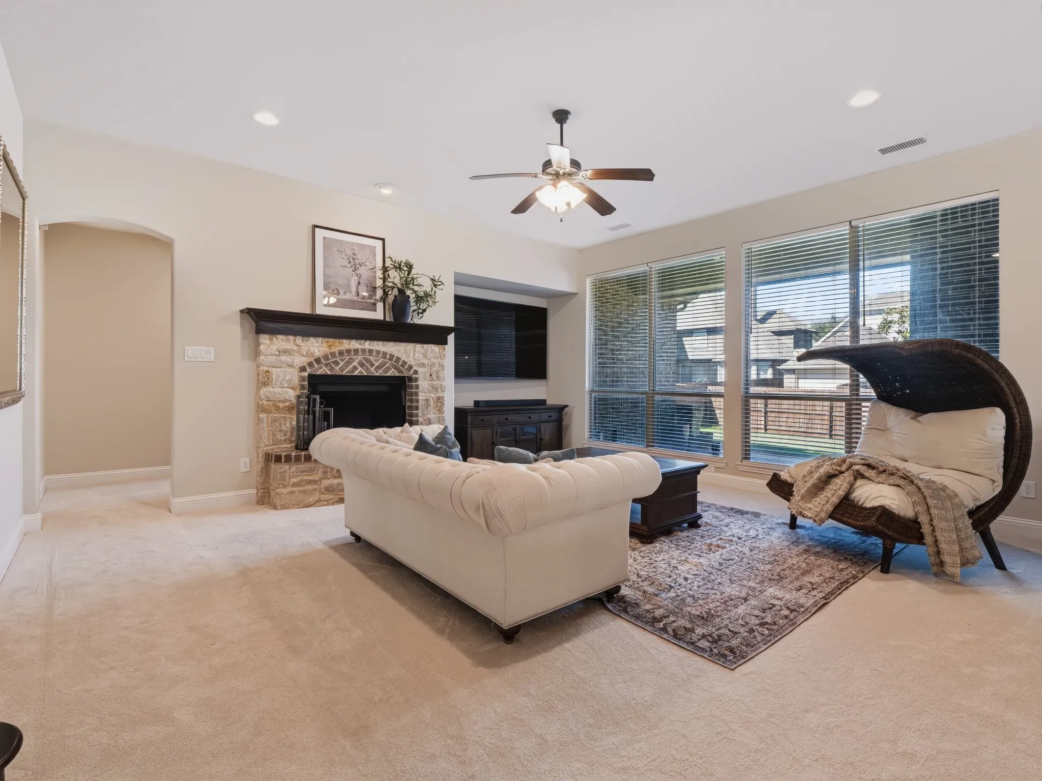 Carpeted flooring, stone fireplace with a dark wood mantel, recessed lighting, ceiling fan, and large windows