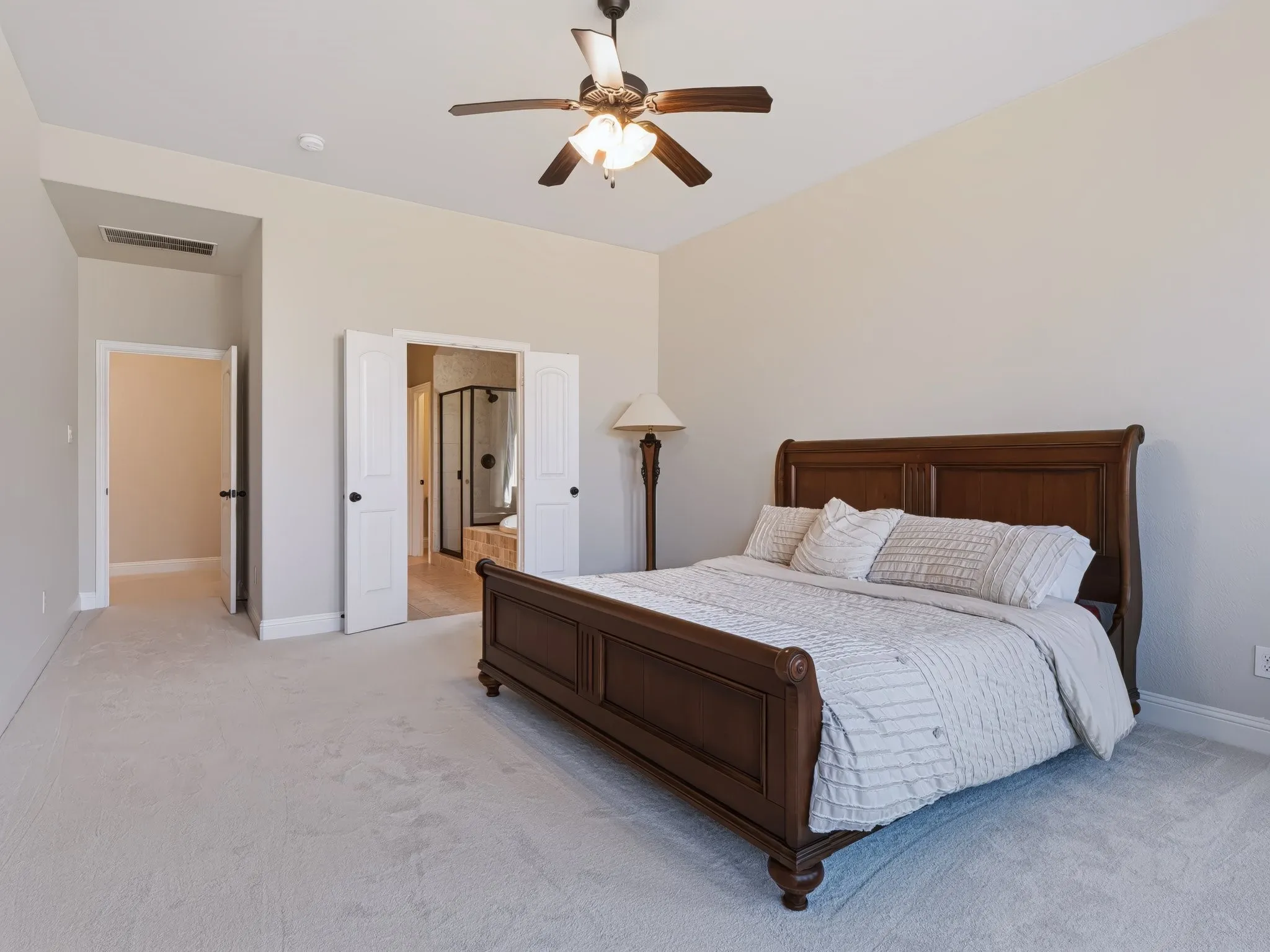 Carpeted flooring, vaulted ceiling, ceiling fan with integrated lighting, double doors, and an en-suite bathroom with a glass-enclosed shower