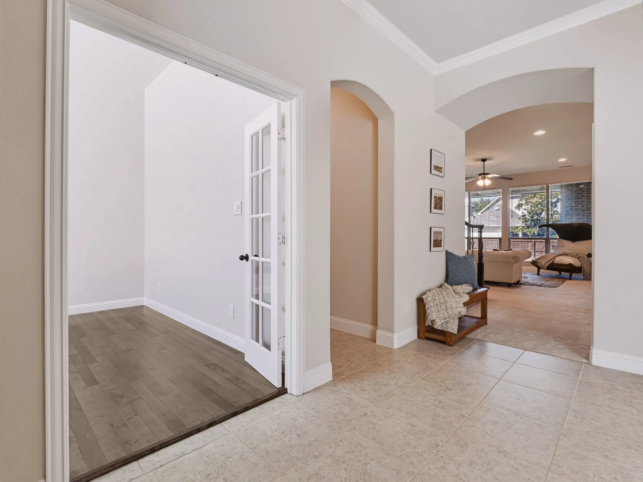 Entryway featuring ceramic tile flooring, arched doorways, crown molding, and a room with wood-finish flooring and French doors