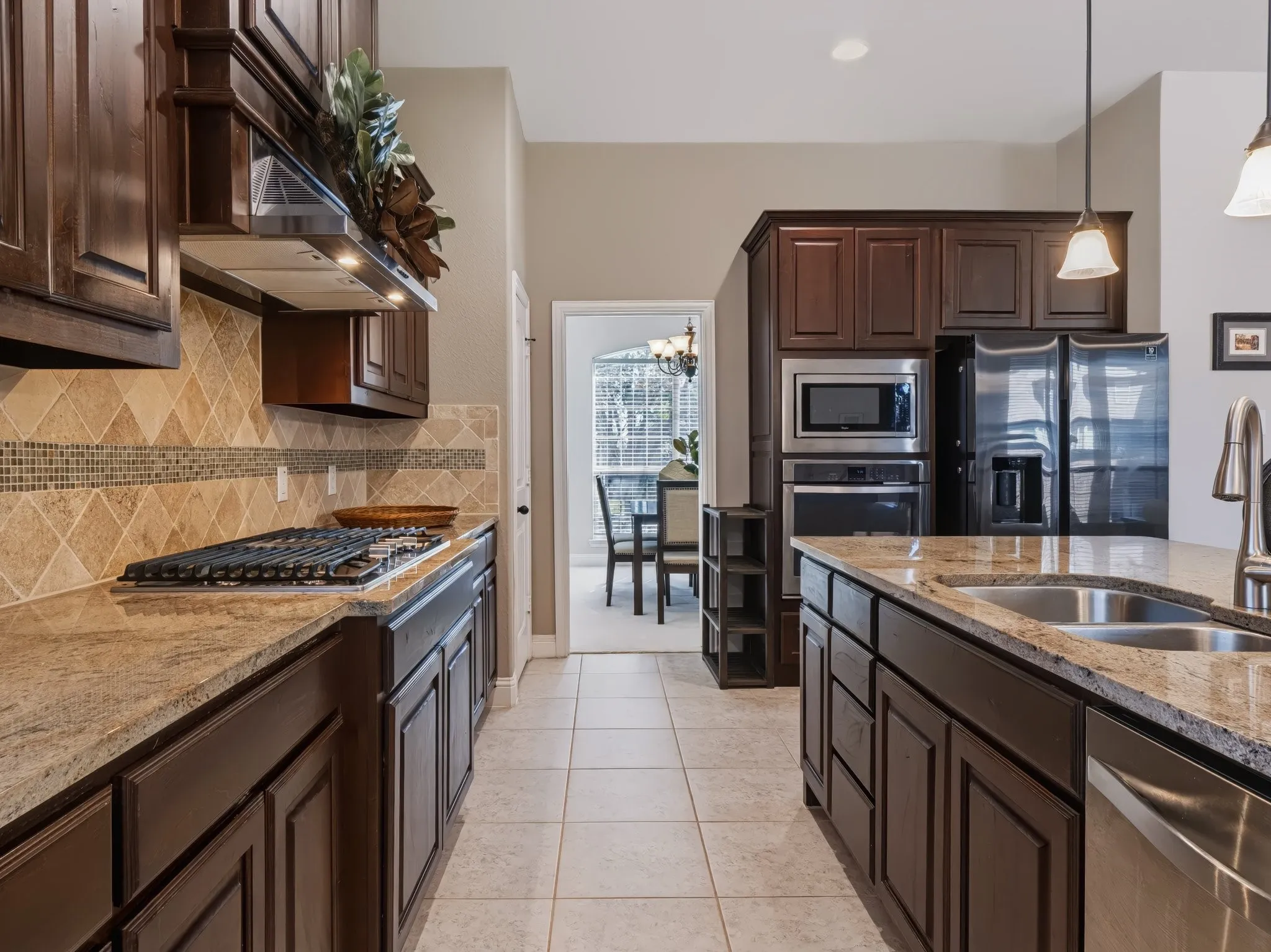 Kitchen featuring dark wood cabinetry, light-toned granite countertops, a tiled backsplash, and stainless steel appliances