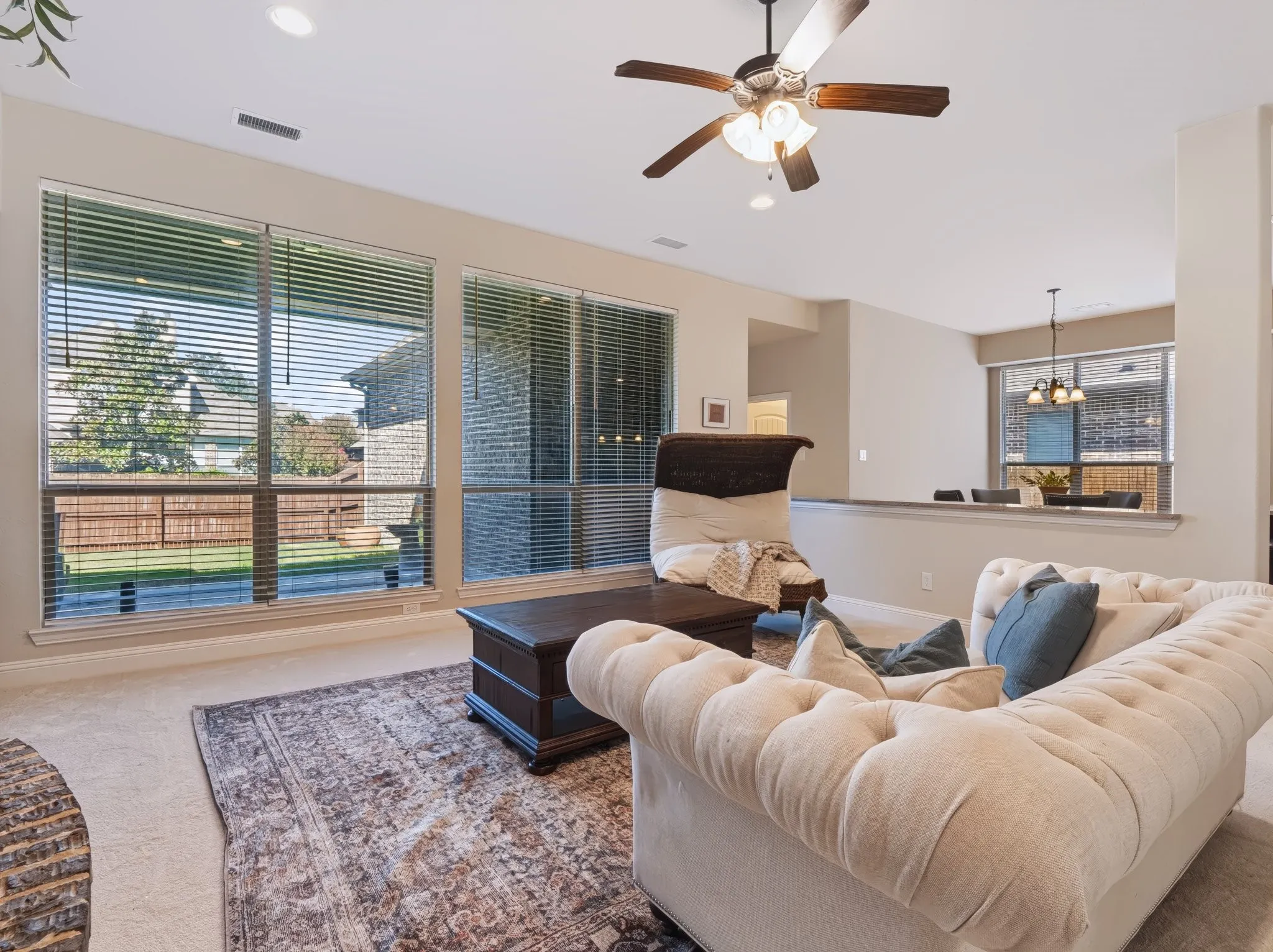 Recessed lighting, ceiling fan with wood-finish blades, and multiple windows with blinds