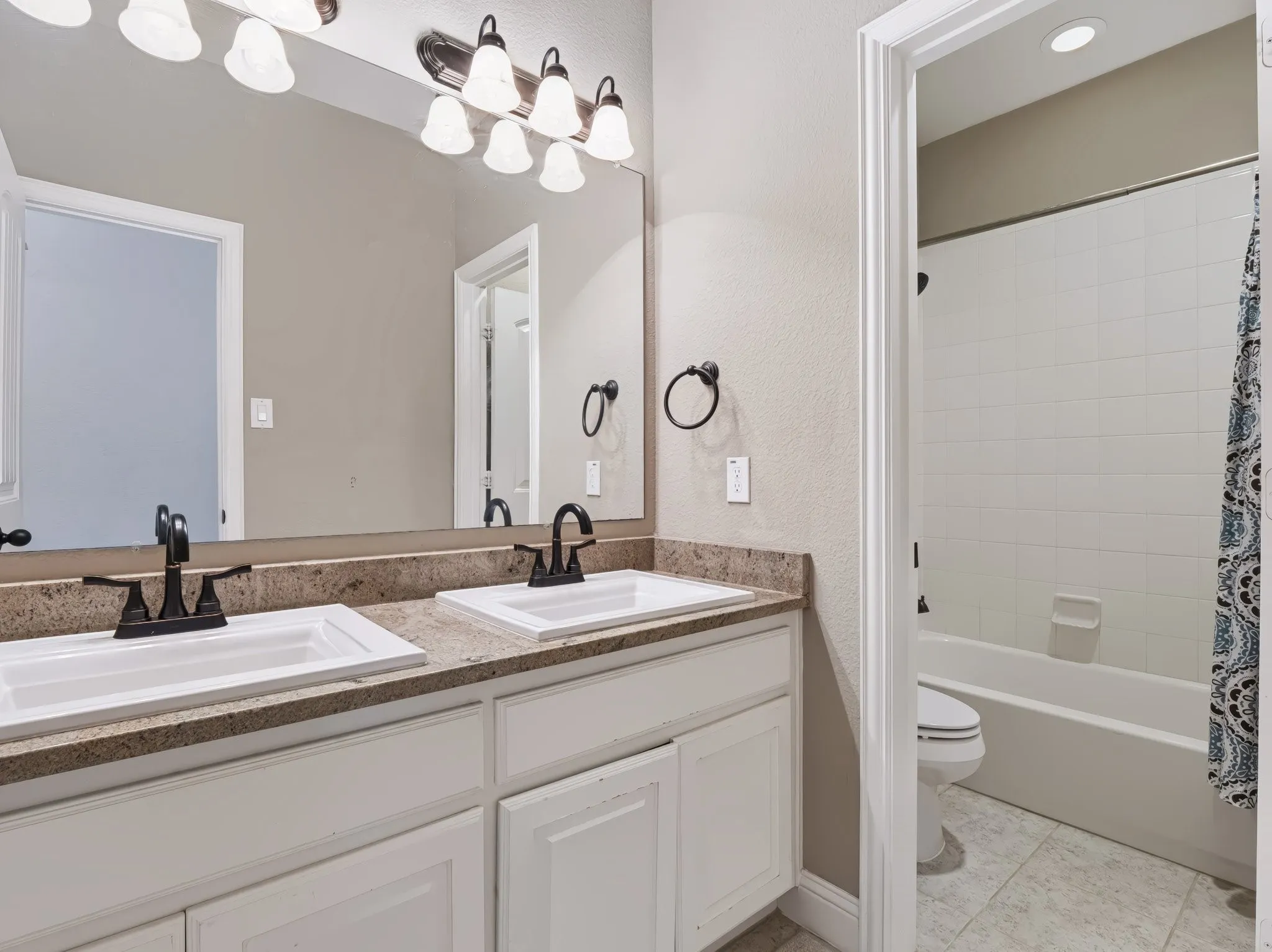 Dual vanity with white cabinetry, speckled countertop, and dark-finish faucets