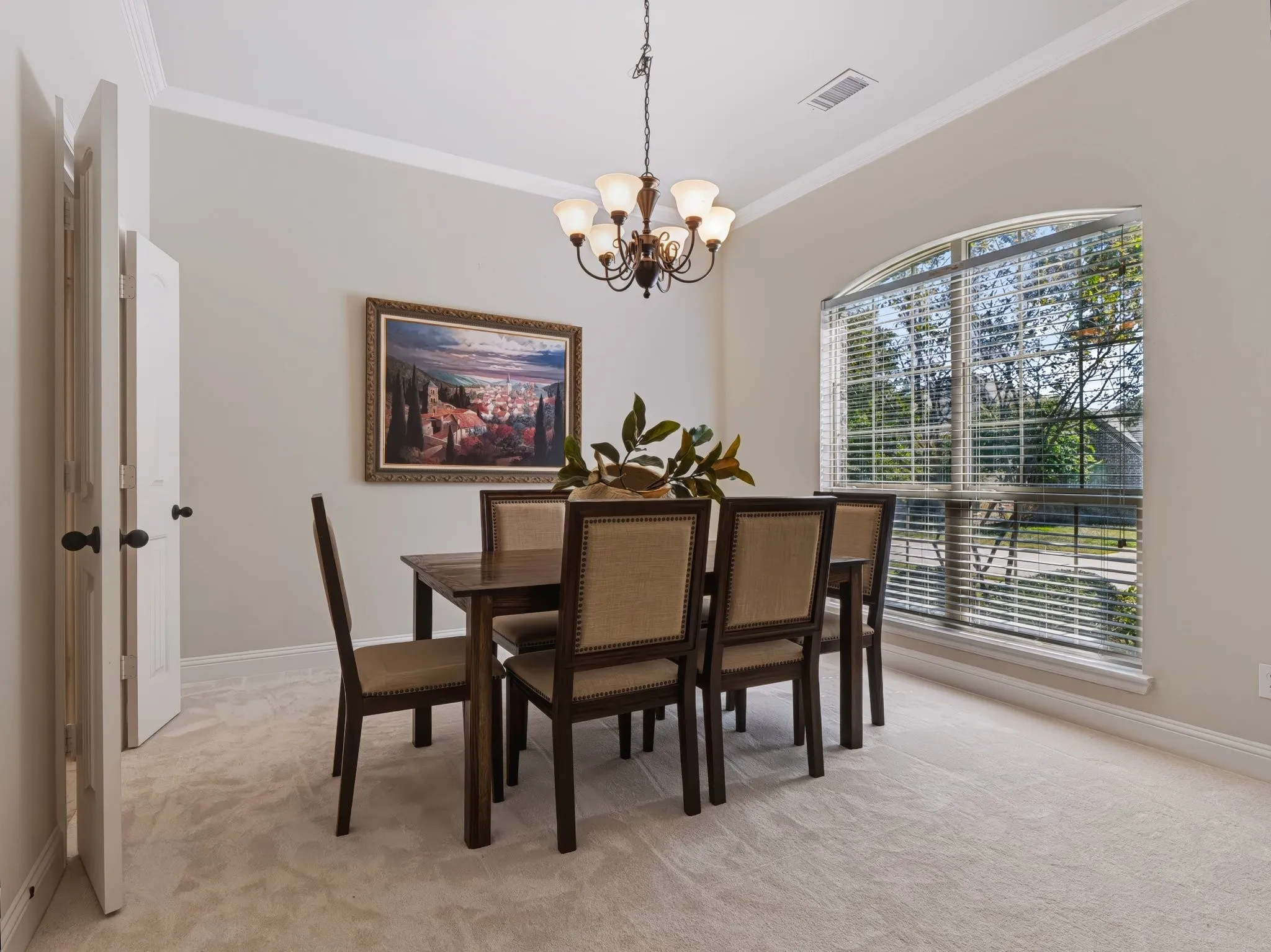 Arched window with blinds, carpeted flooring, crown molding, and a five-light chandelier
