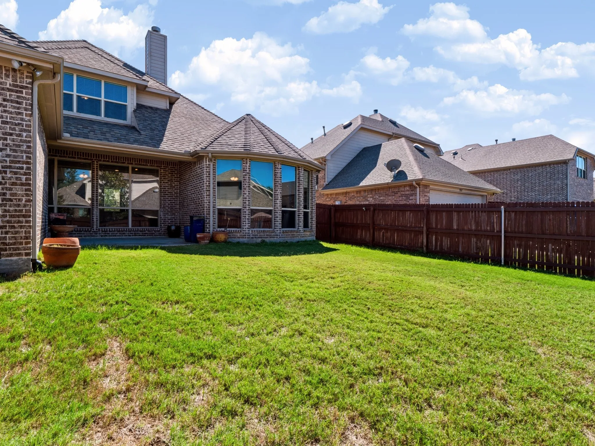 Expansive backyard featuring a manicured lawn, a full brick exterior, a large bay window, a concrete patio, and a privacy fence