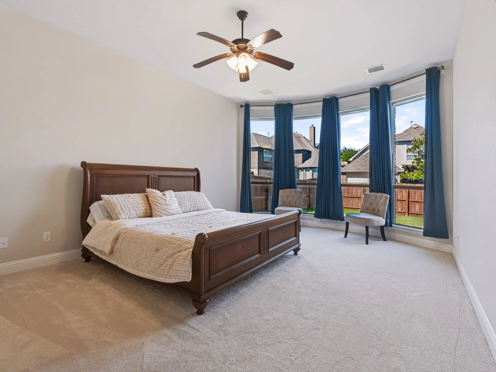 Tray ceiling with a ceiling fan, light-toned carpeting, and a bay window