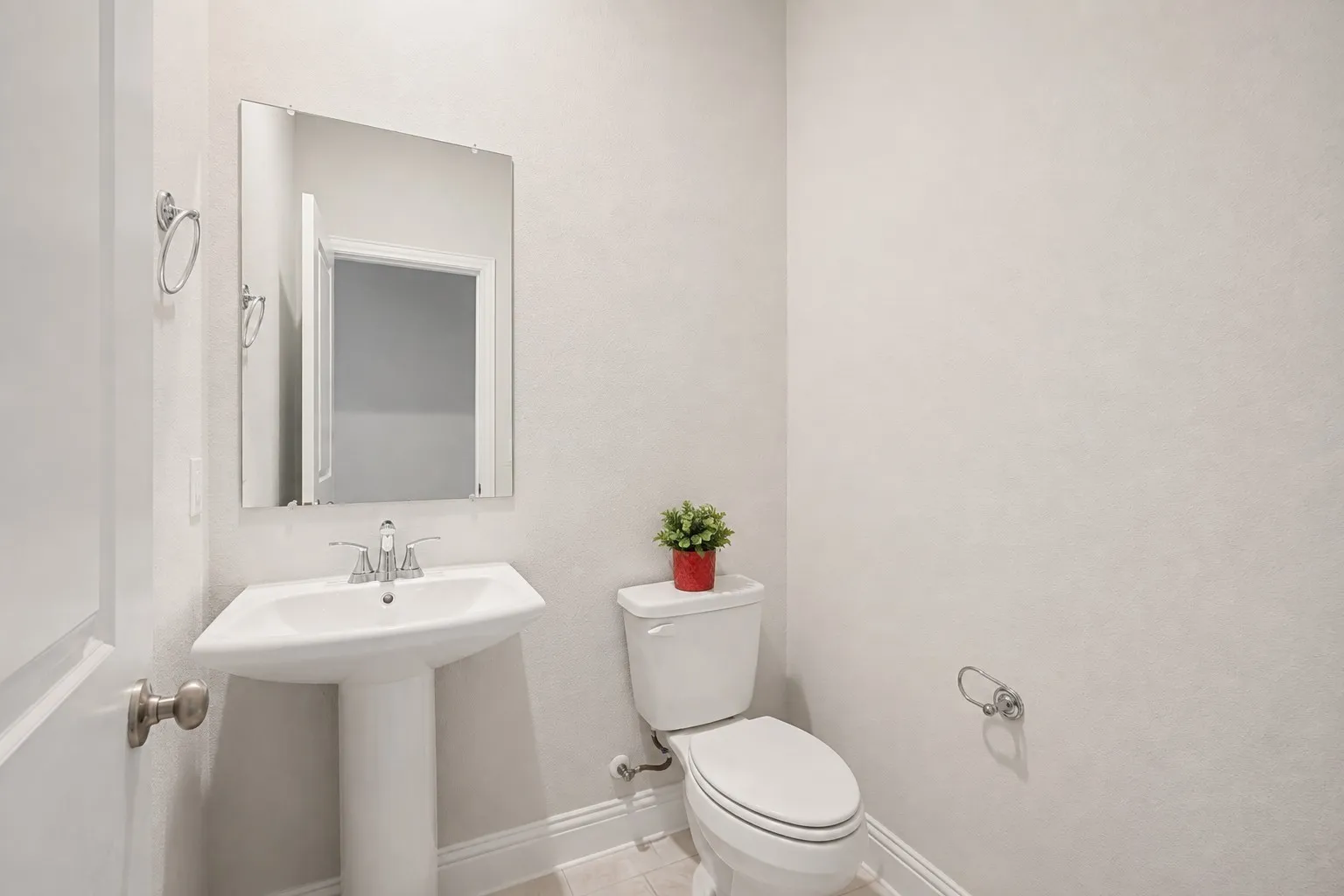 Pedestal sink with chrome faucet, wall-mounted mirror, and white toilet
