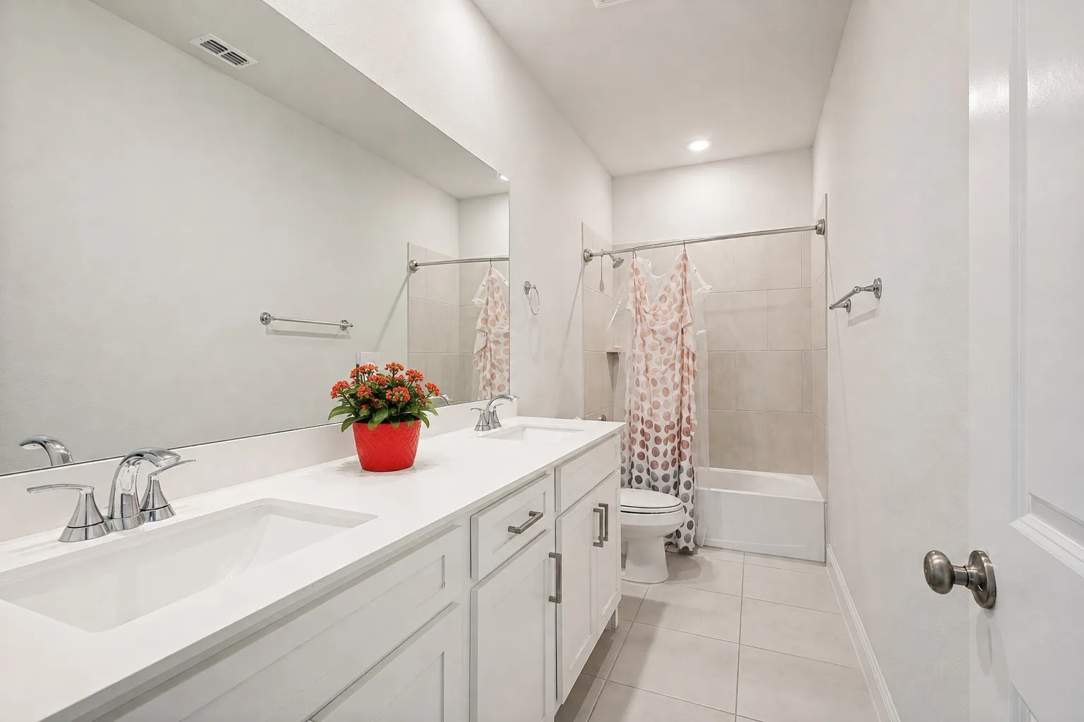 Dual vanity with chrome fixtures and integrated sinks, a full-width mirror, light-toned floor tiling, and a bathtub with a tiled surround