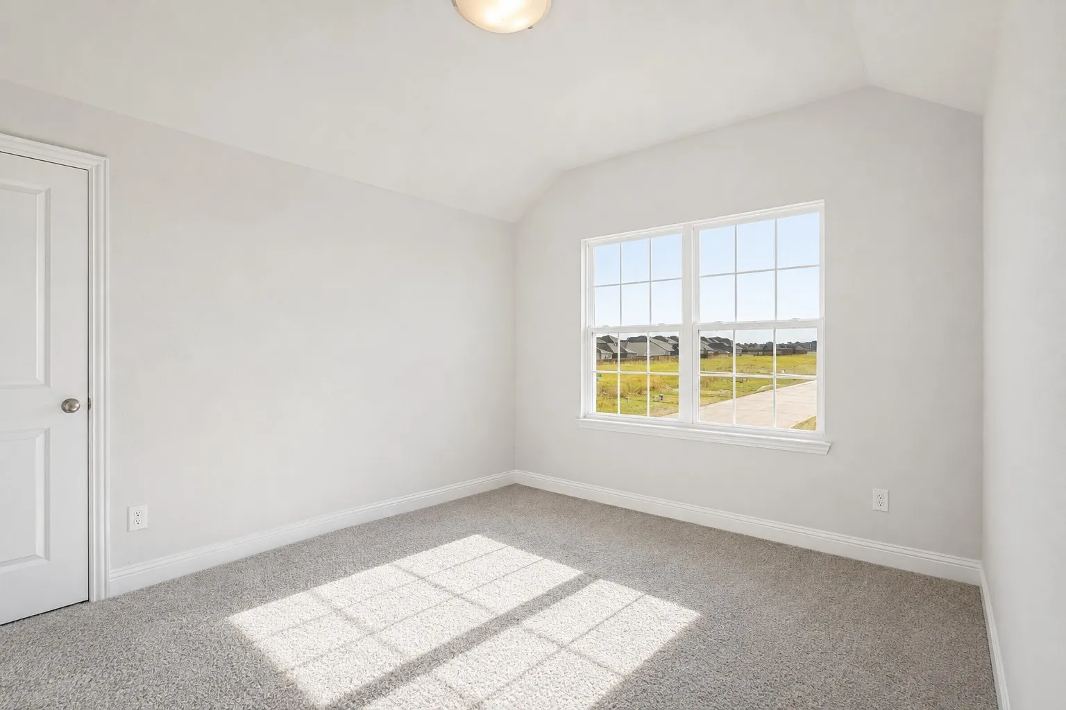 Vaulted ceiling, double-hung window with grilles, light gray carpet, white interior door, and flush mount ceiling light
