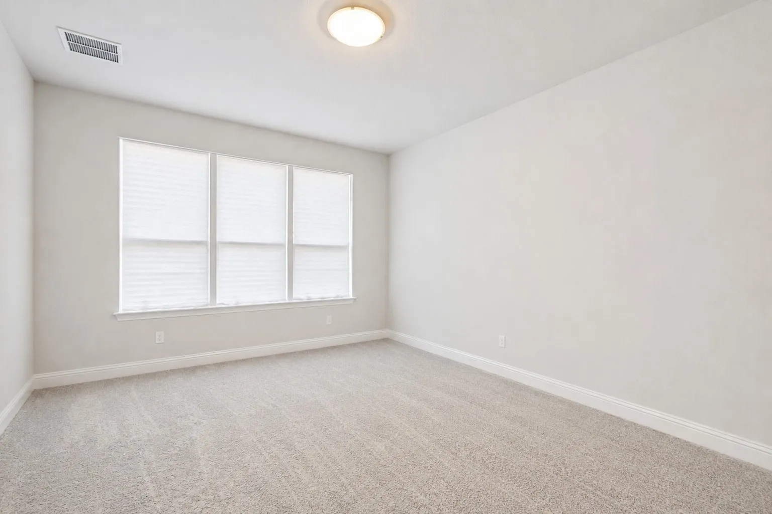 Neutral-toned wall paint, plush carpet flooring, three large windows, and a flush mount ceiling light fixture