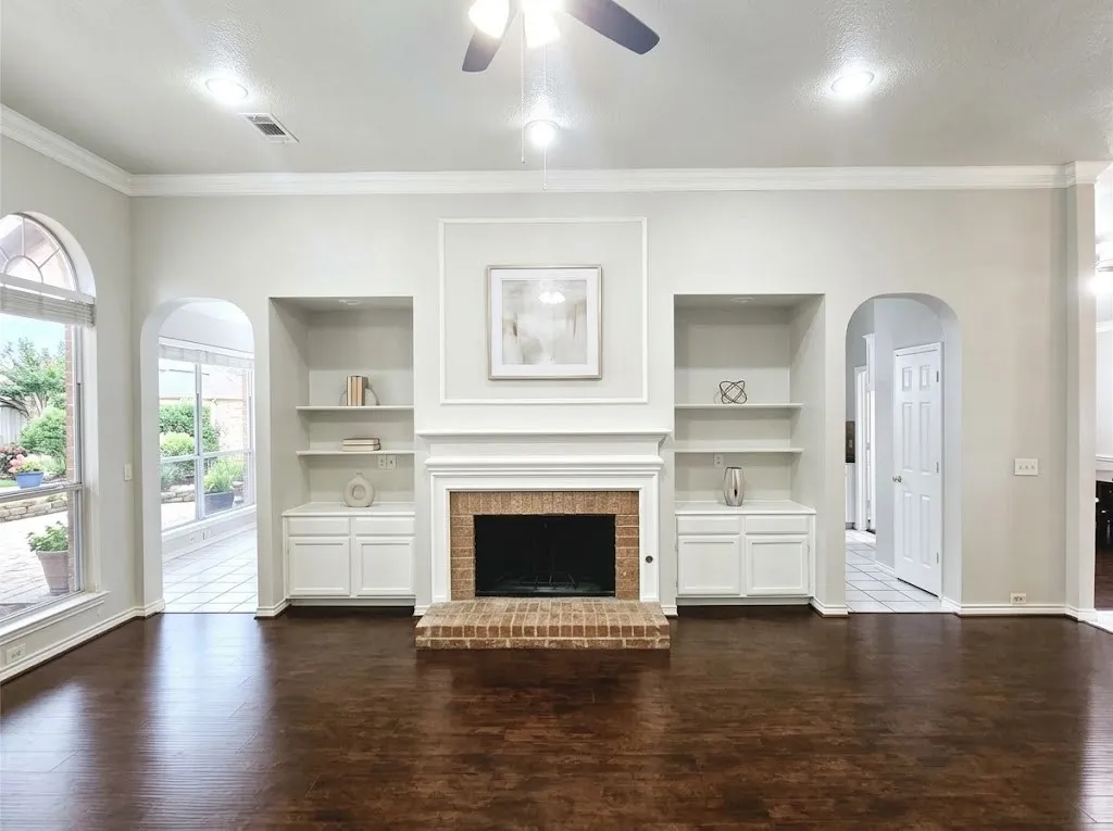 Brick fireplace with white mantel and hearth, built-in shelving and cabinetry, wood-finish flooring, and recessed ceiling lighting