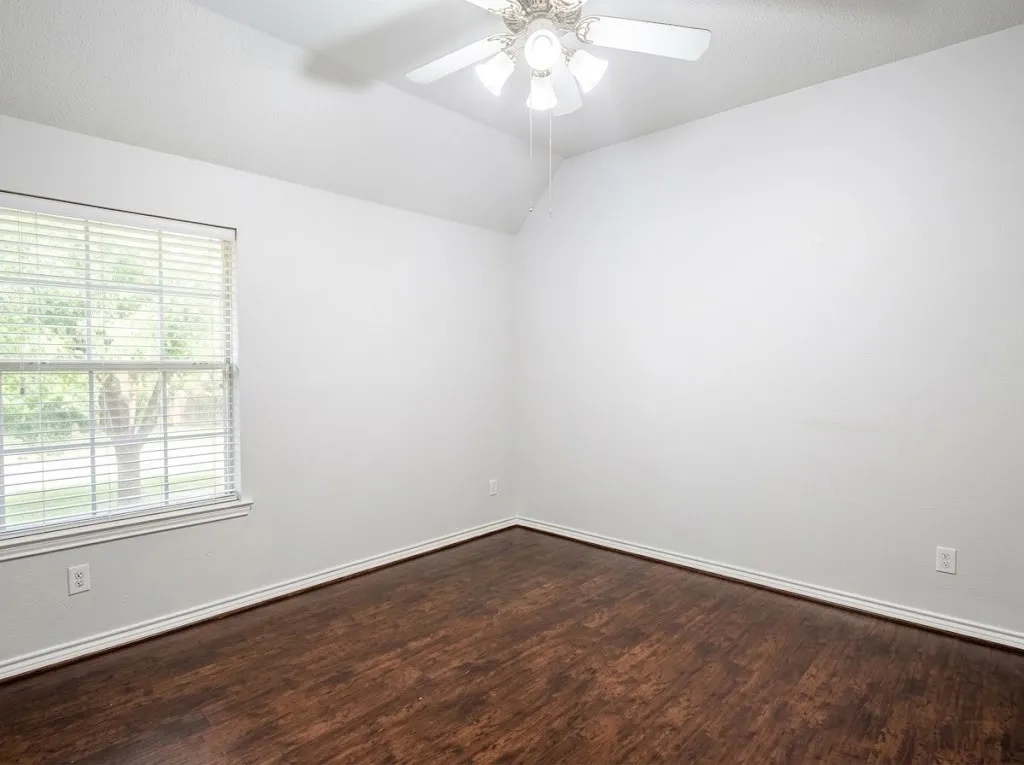 Vaulted ceiling with a ceiling fan, wood-finish flooring, and a large window with blinds