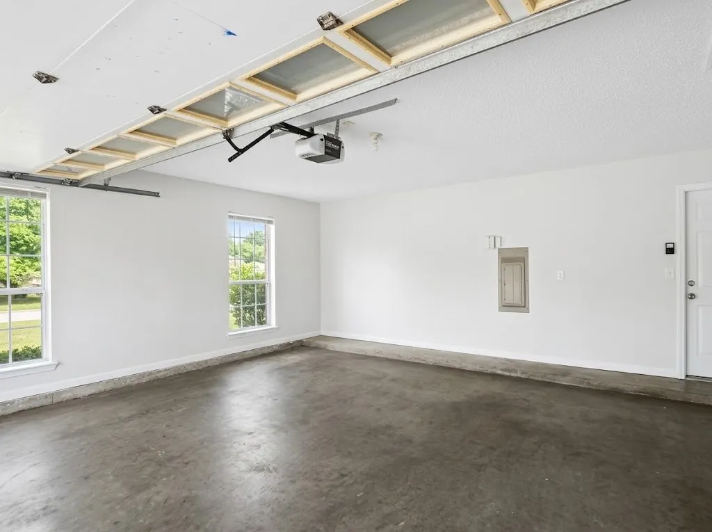 Attached garage with concrete flooring, two windows, and overhead garage door mechanism