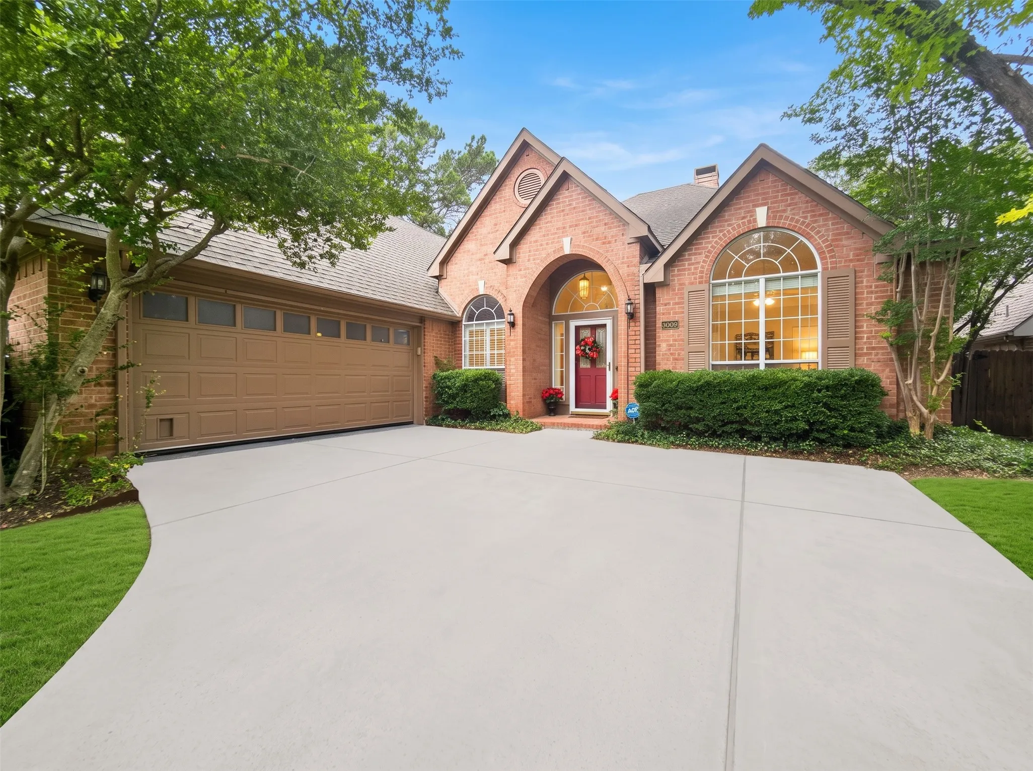 Brick facade, arched entry, arched window with shutters, multi-pane garage door, and a concrete driveway