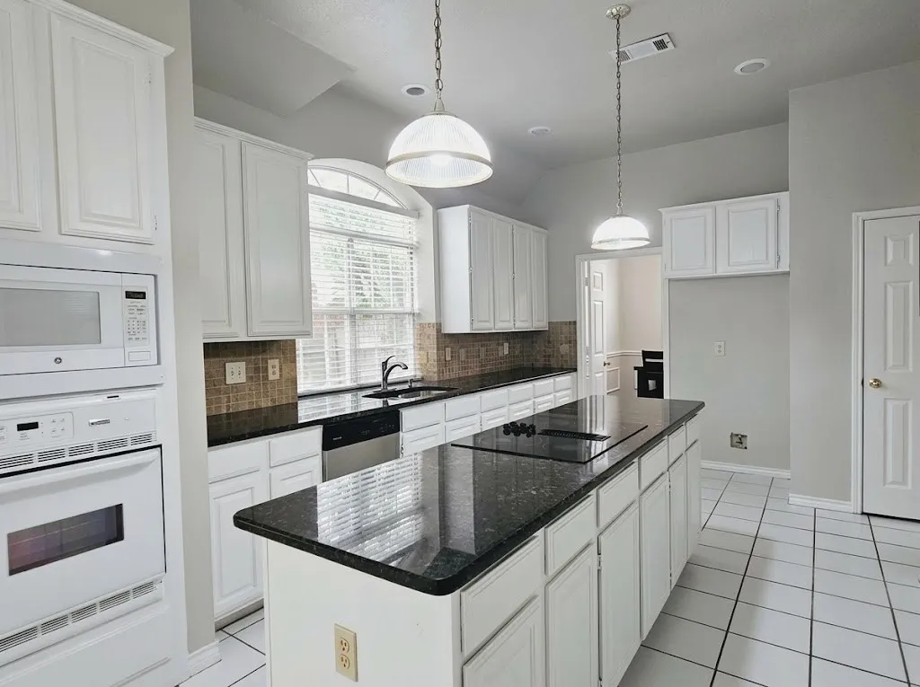 Kitchen featuring white cabinetry, dark stone countertops, an integrated cooktop, and built-in appliances