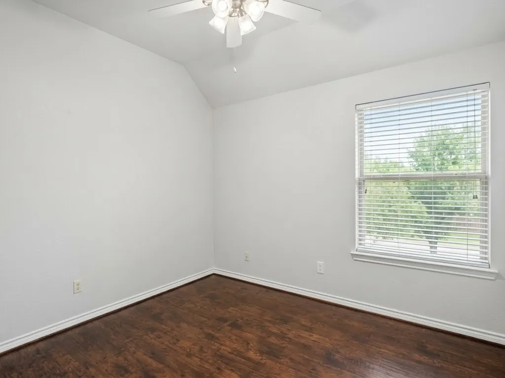 Hardwood-look flooring with white trim, vaulted ceiling, and ceiling fan