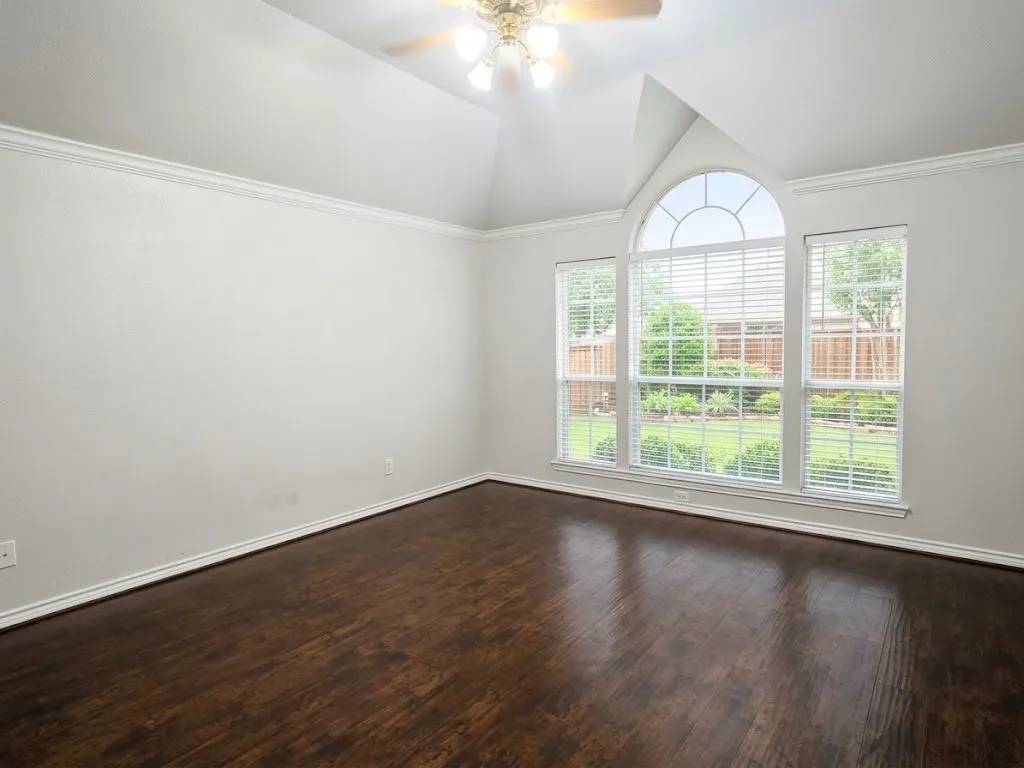 Vaulted ceiling with crown molding, wood-finish flooring, and arched window