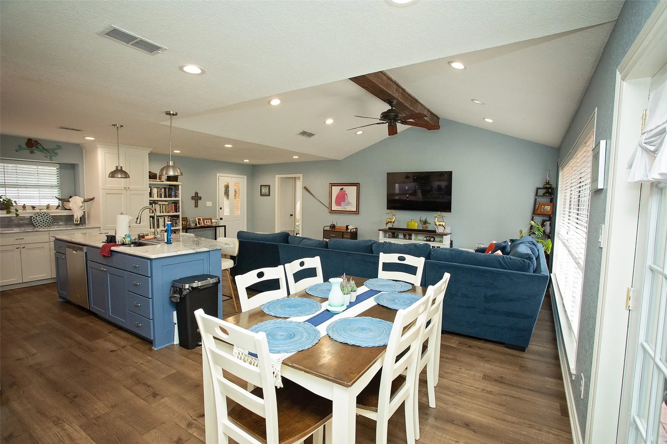 Open concept living space featuring wood-finish flooring, vaulted ceiling with exposed beam, recessed lighting, and a kitchen island with built-in cabinetry