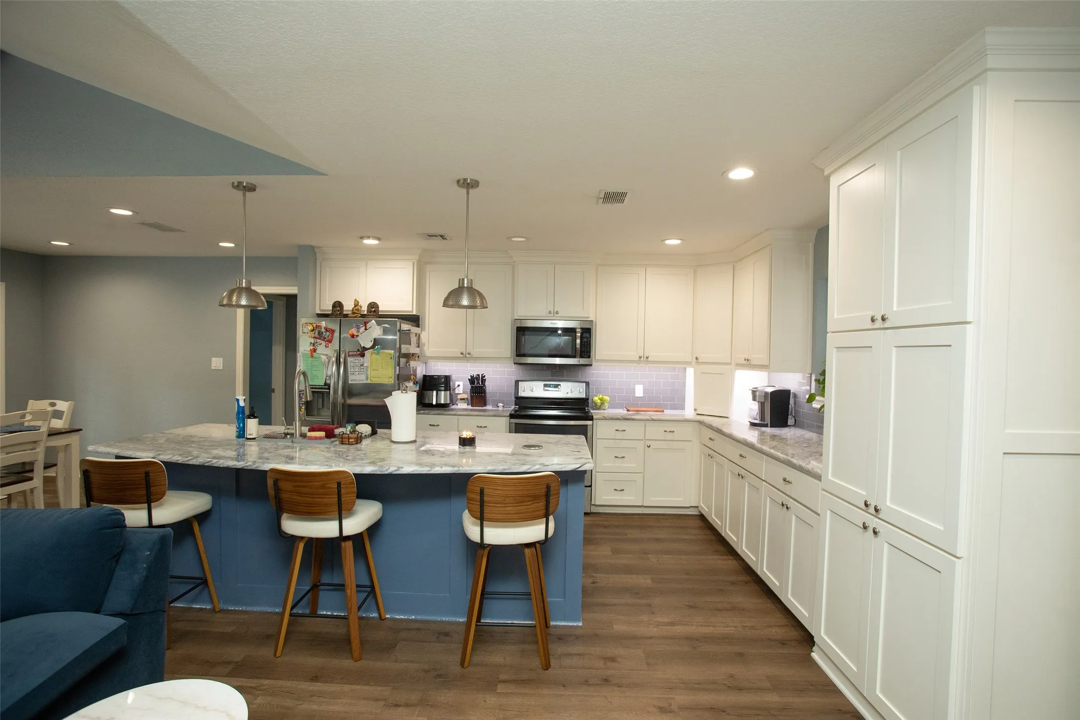 Kitchen featuring white shaker cabinetry, an island with a blue base and light-toned countertop, wood-finish flooring, recessed lighting, and stainless steel appliances