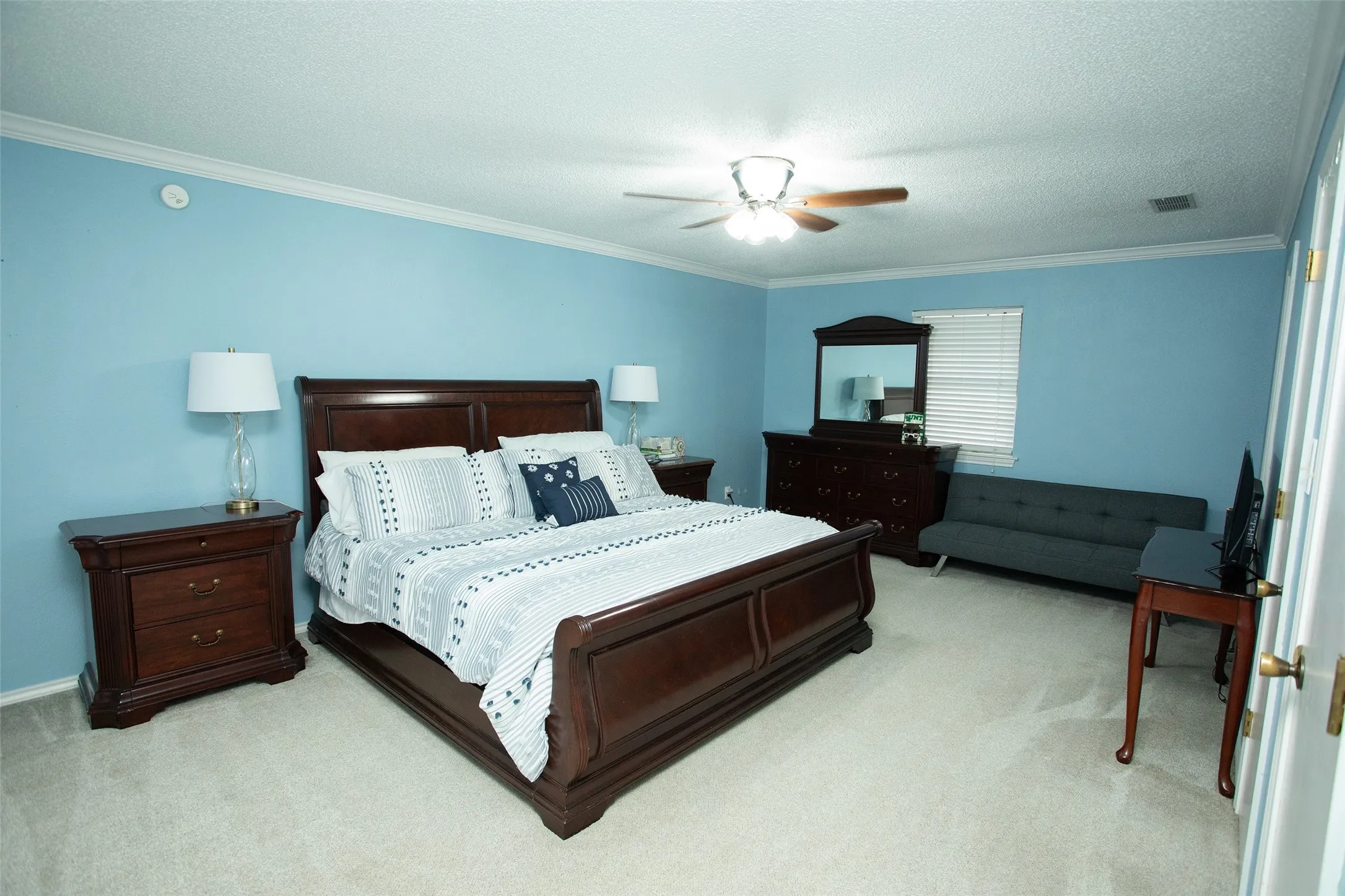 Plush carpet flooring, crown molding, ceiling fan with integrated lighting, window with horizontal blinds, and a built-in closet with louvered doors