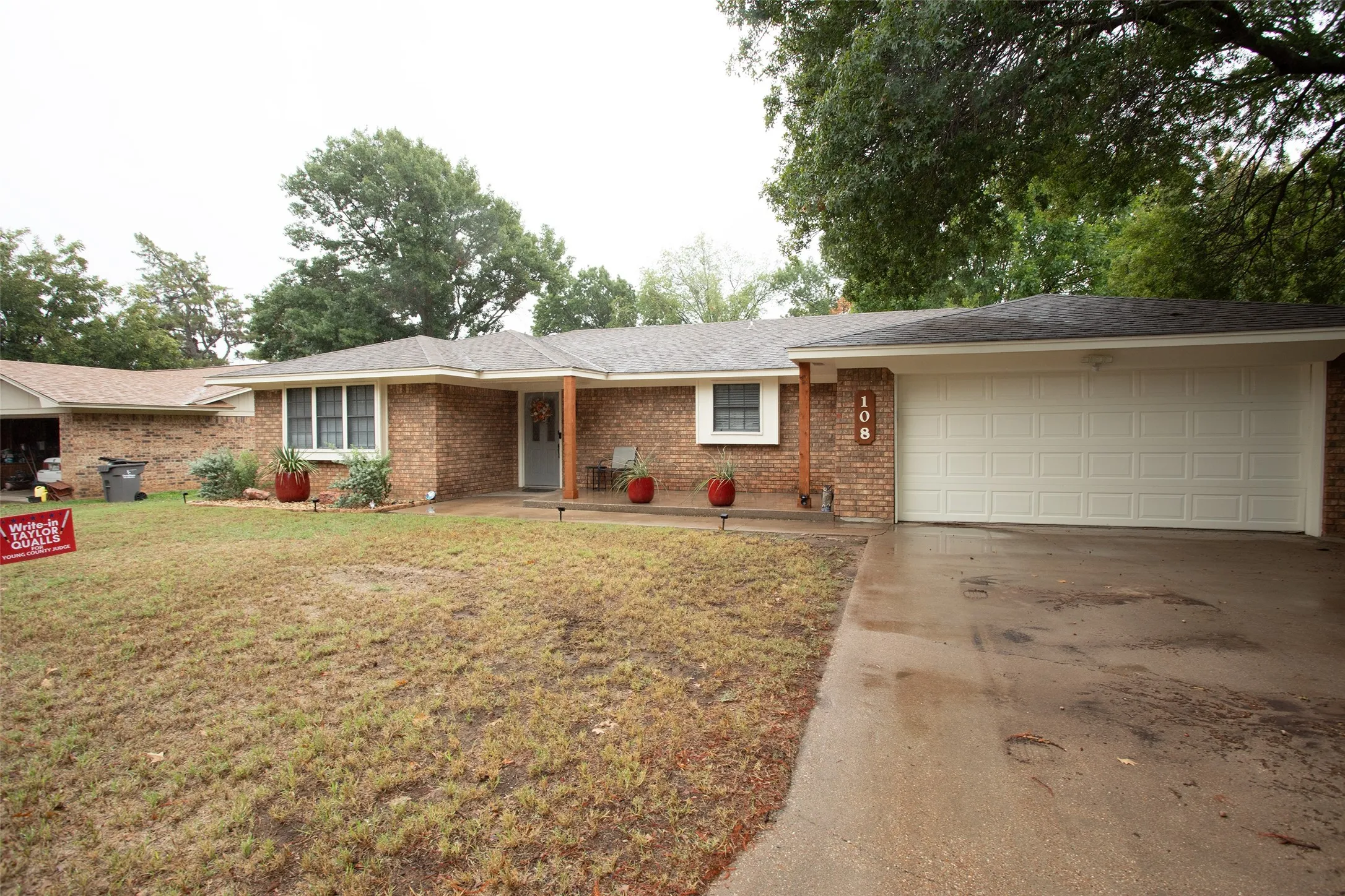 Brick exterior, covered front porch, white-paneled garage door, exposed wood porch column, and a concrete driveway