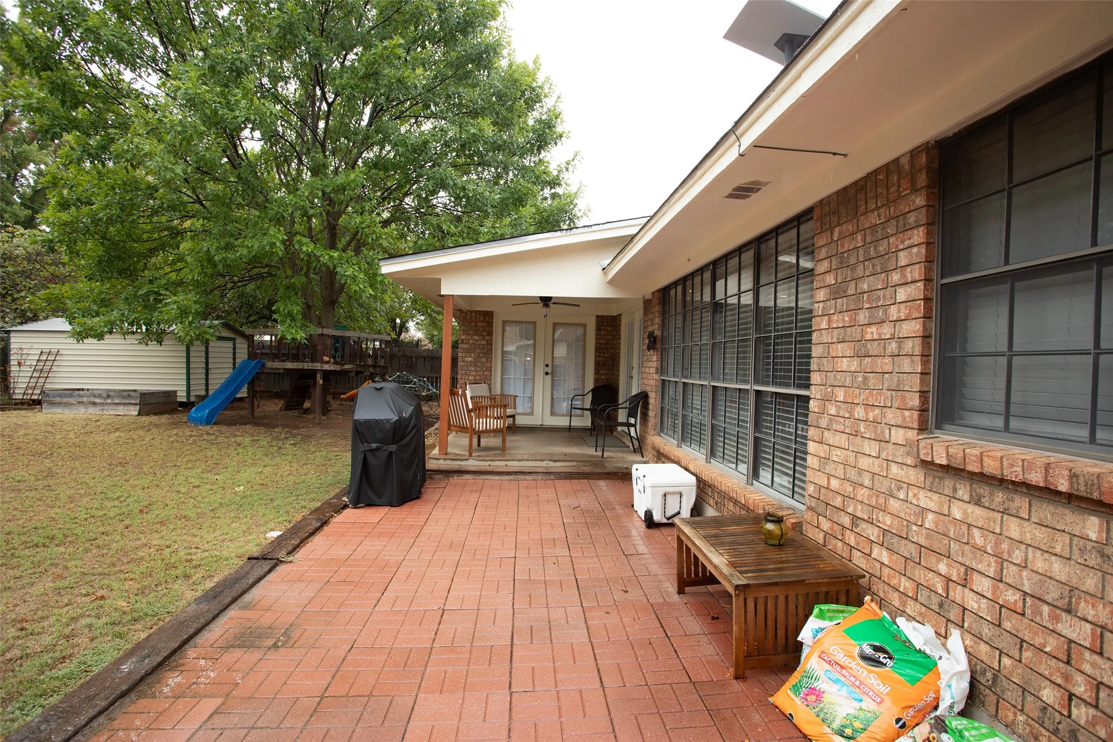 Brick exterior with large grid-pattern windows, covered patio with brick paver flooring, and double French doors