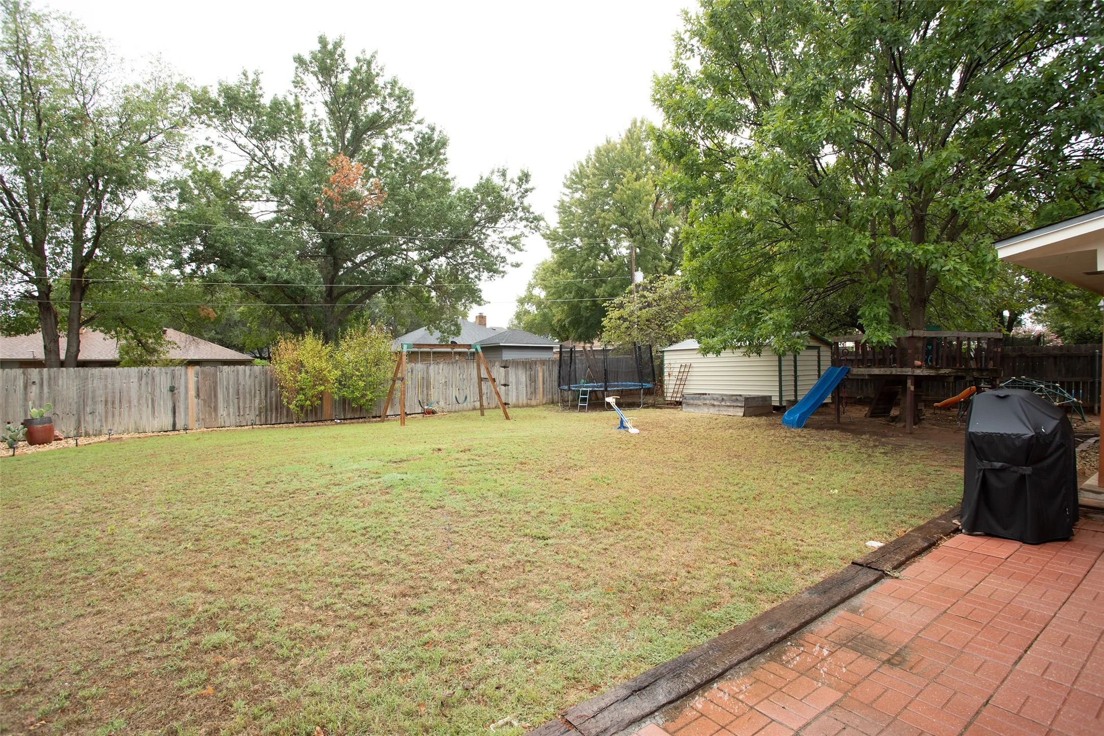 Expansive backyard featuring a red brick patio, mature trees, and privacy fencing