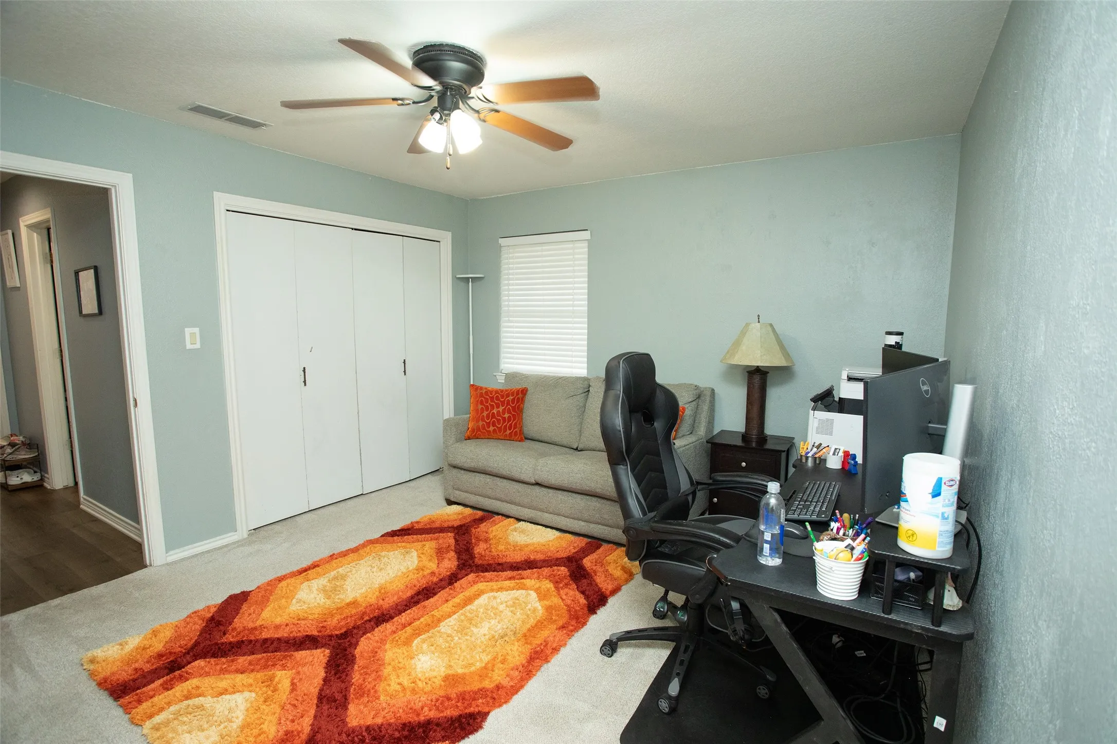 Ceiling fan with light fixture, carpeted flooring, window with blinds, bi-fold closet doors, and a wood-finish doorway