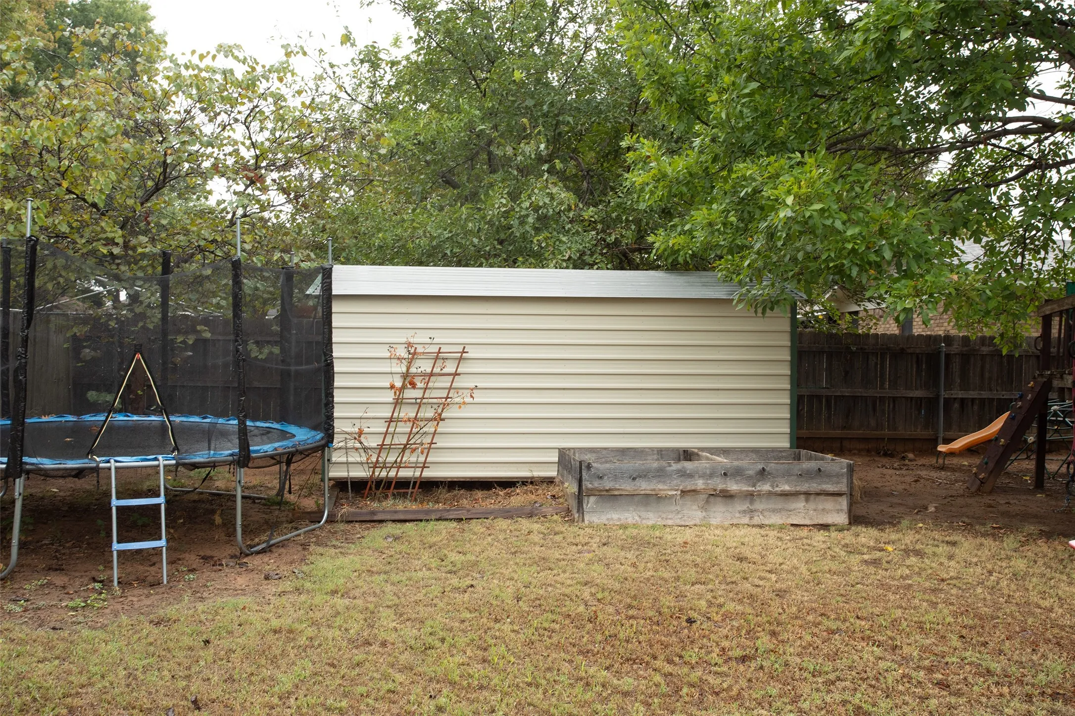 Backyard featuring a metal storage shed, wood fence, and mature trees