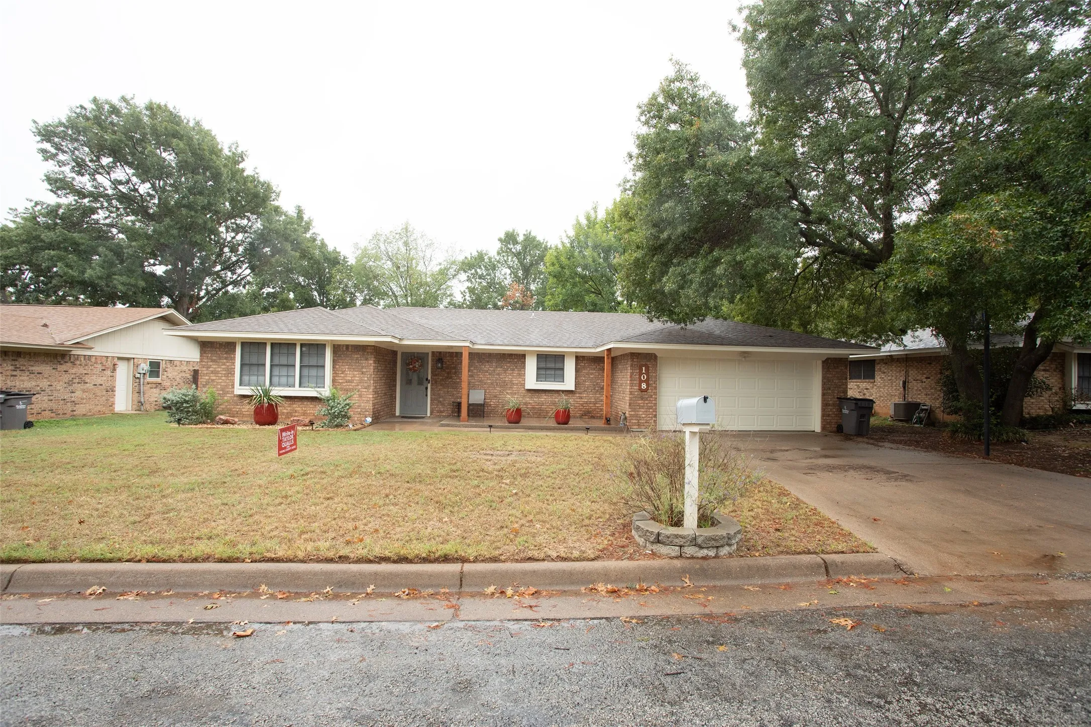 Brick exterior with a gabled roofline, attached garage, and mature trees