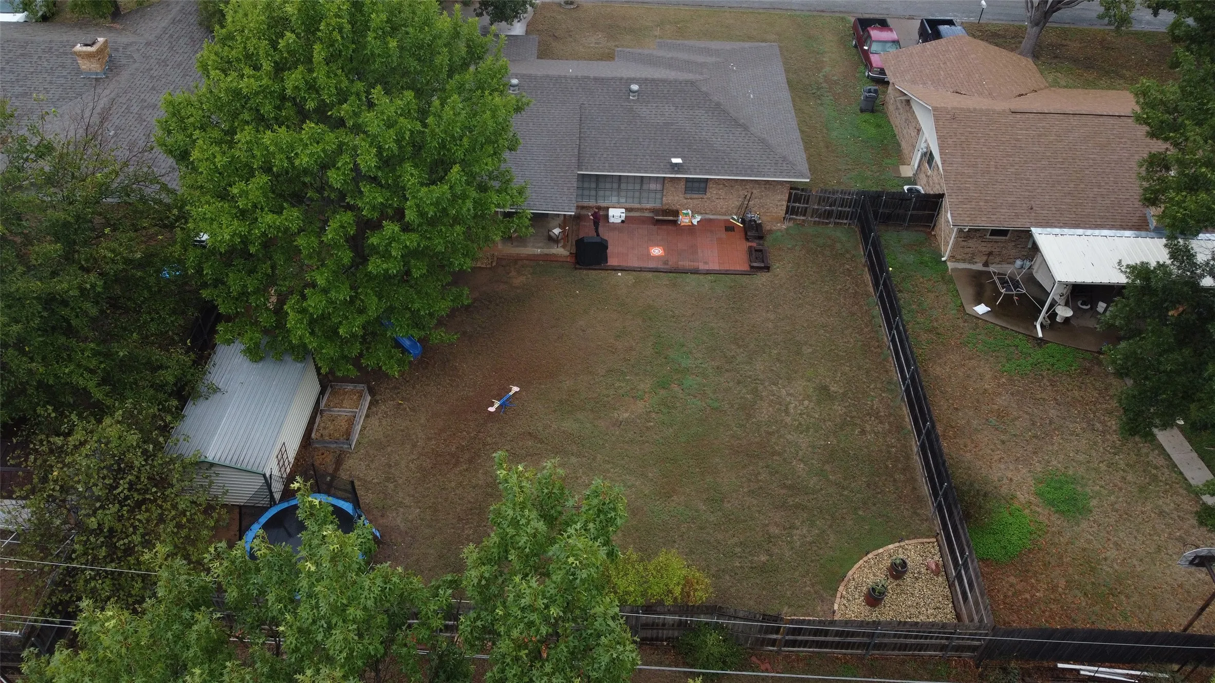 Expansive backyard featuring a wood deck, perimeter fencing, mature trees, and a storage shed