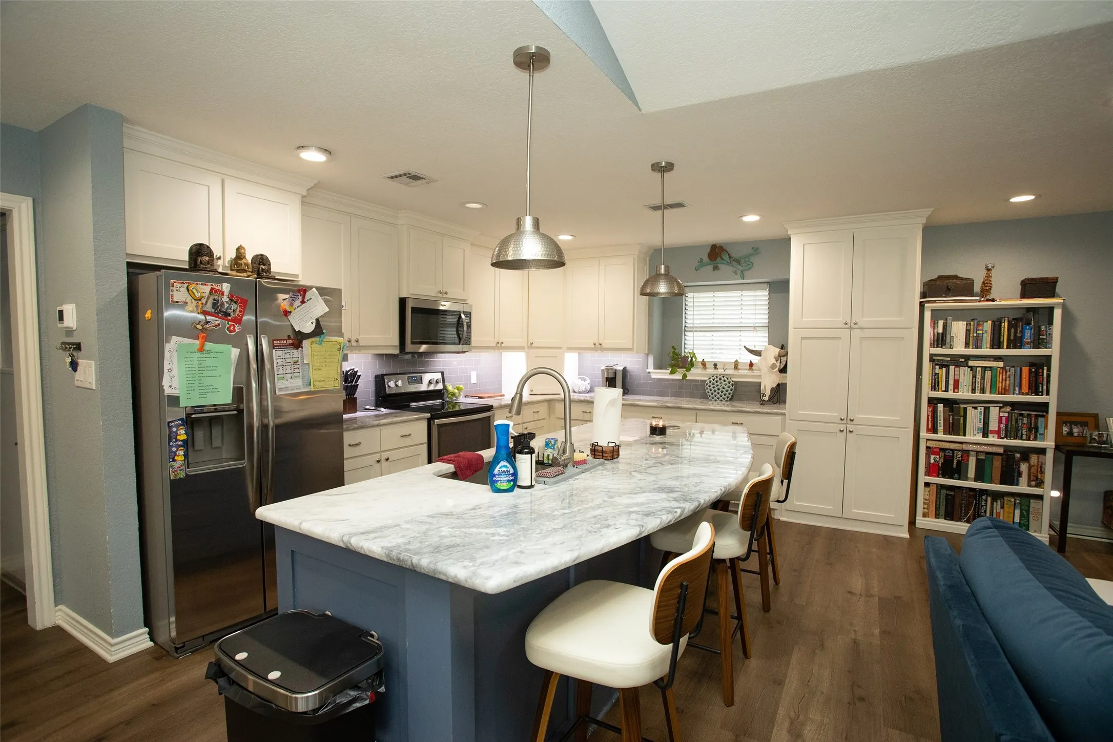 Kitchen featuring a large island with stone countertop, stainless steel appliances, white cabinetry, wood-finish flooring, and recessed lighting