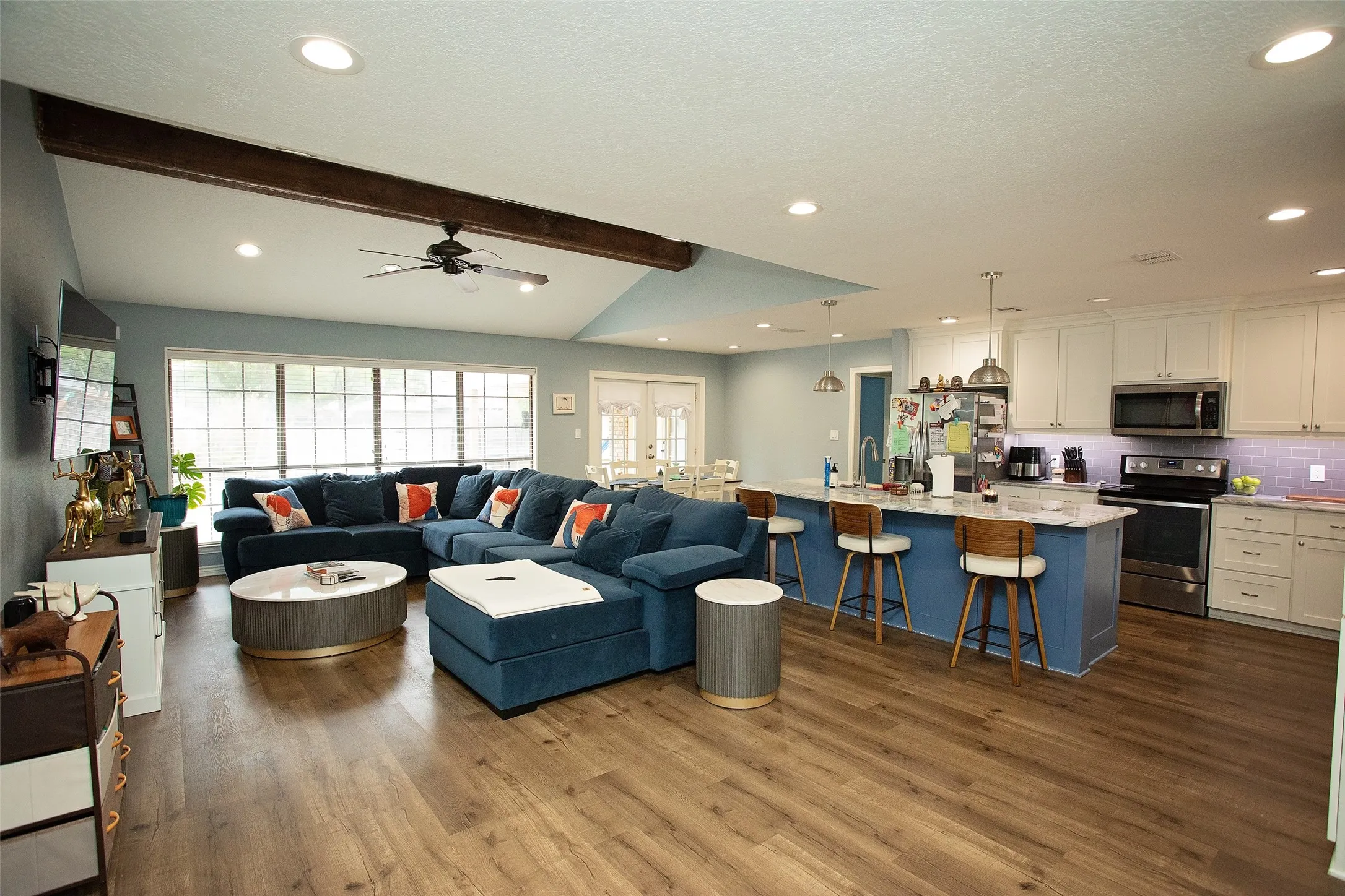 Open-concept living space featuring wood-finish flooring, vaulted ceiling with exposed beam, recessed lighting, and a ceiling fan