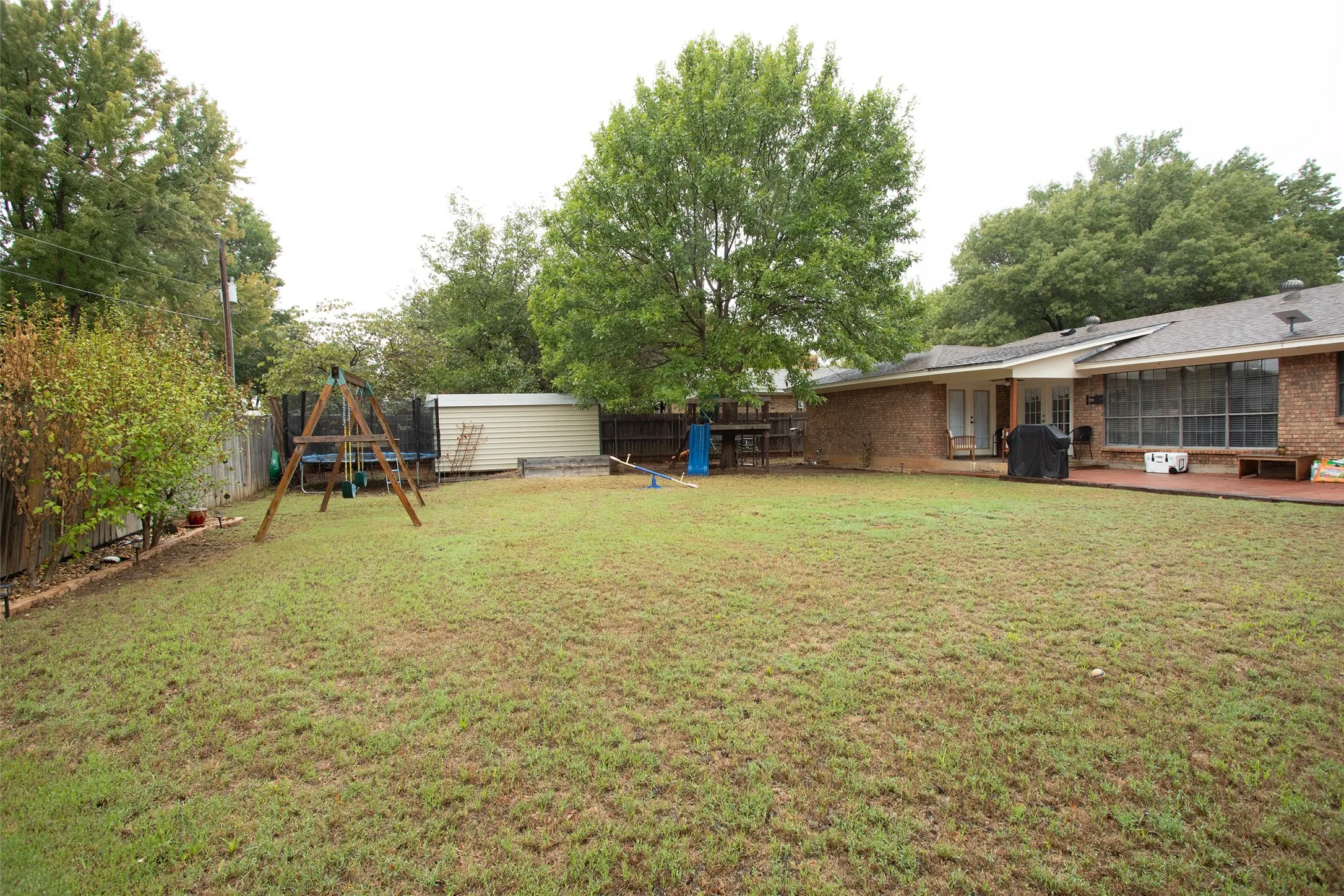 Expansive backyard with a manicured lawn, perimeter fencing, brick exterior, and a large wood-finish deck
