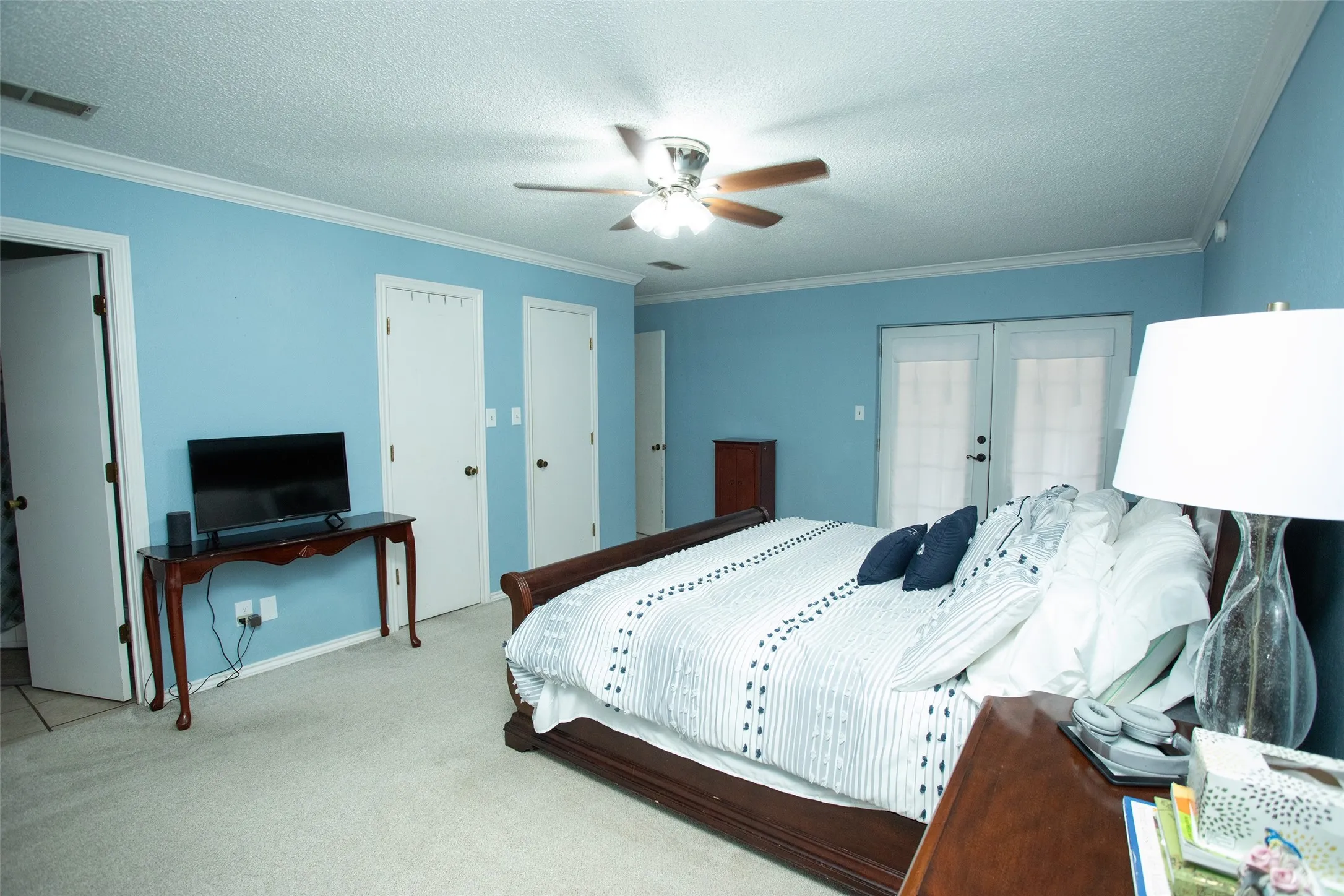 White double French doors, two white interior doors, crown molding, and a ceiling fan with light fixture