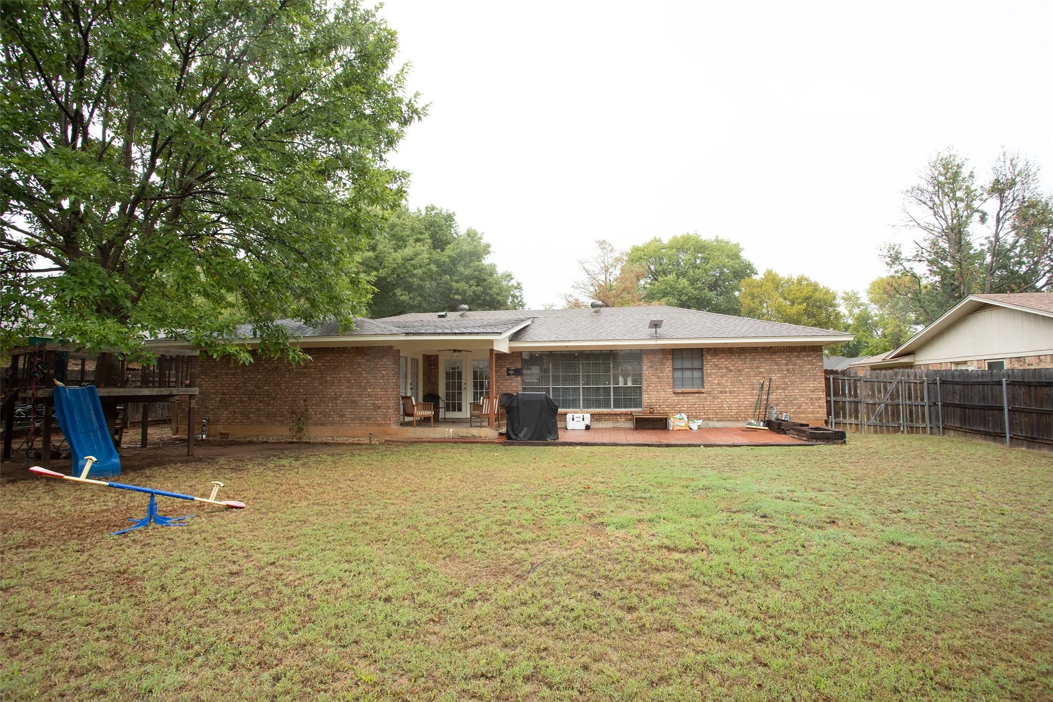Expansive backyard featuring a brick exterior, wood deck, mature trees, and a privacy fence