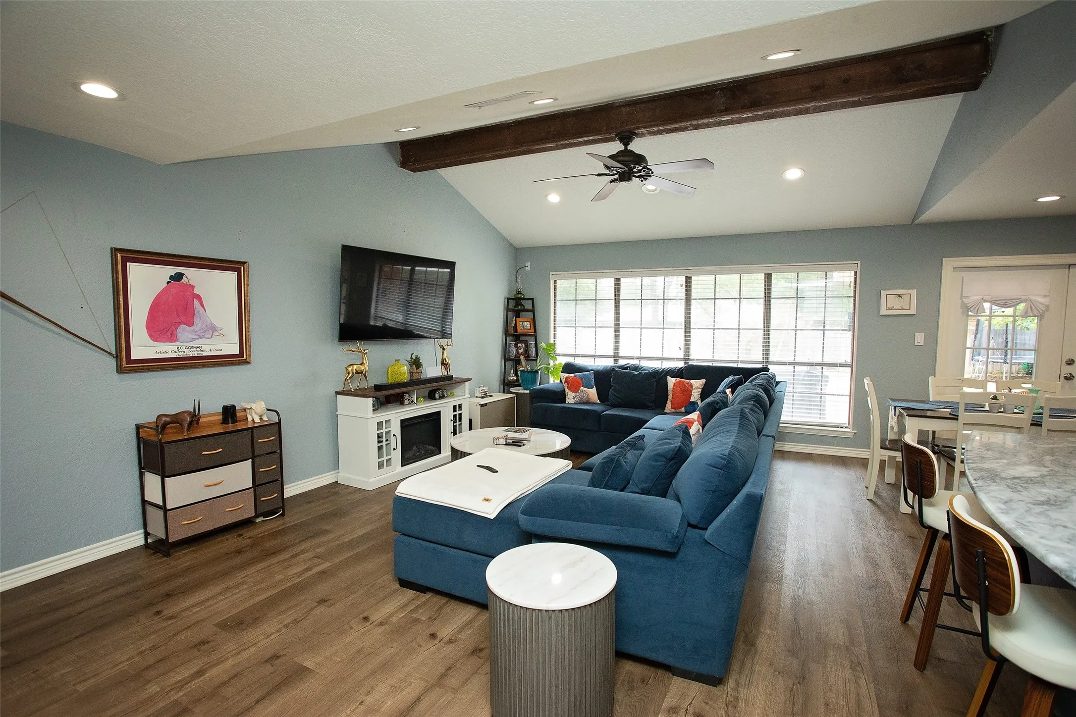 Vaulted ceiling with exposed wood beams, recessed lighting, wood-finish flooring, built-in electric fireplace, and a ceiling fan