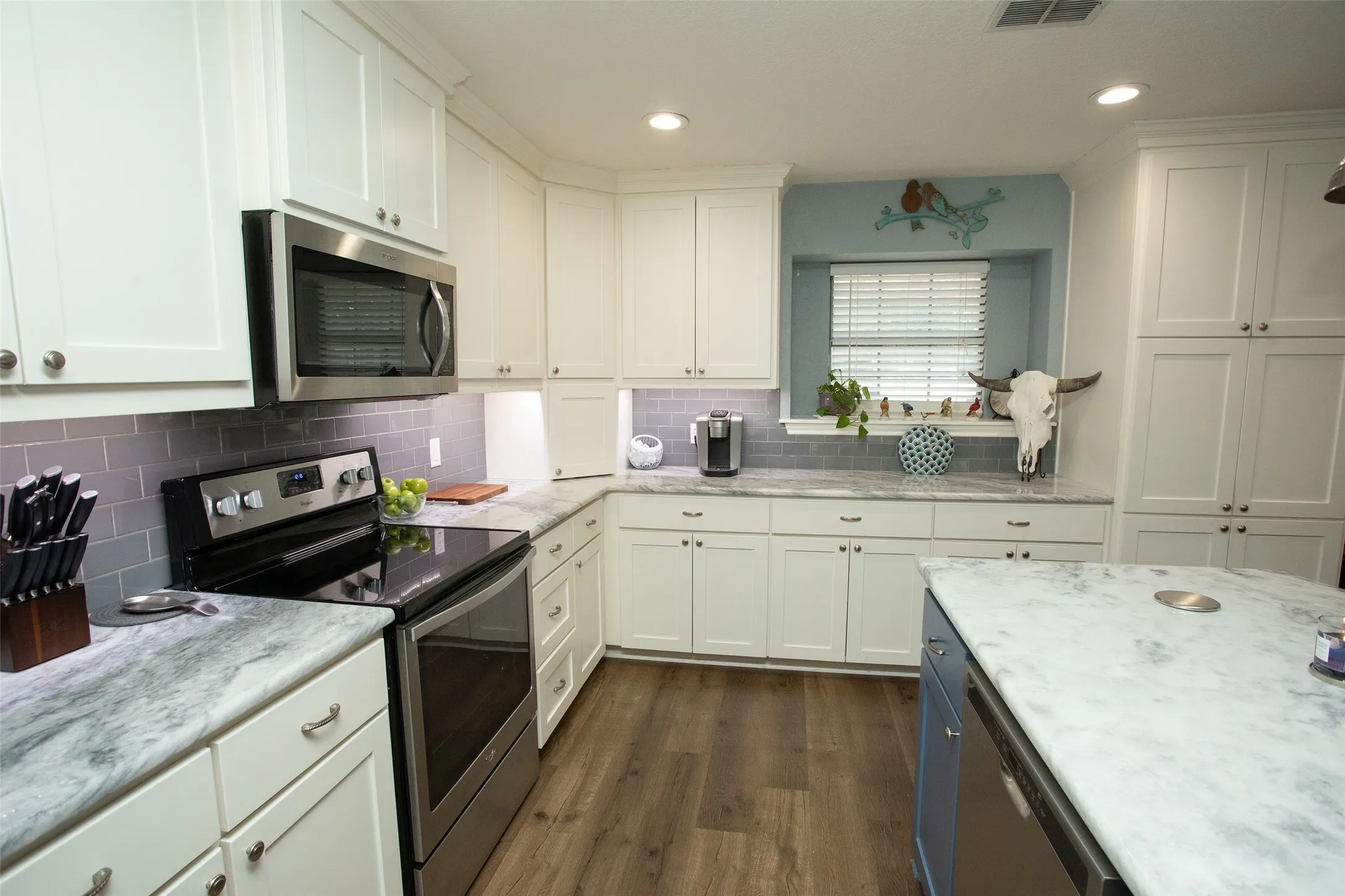 White shaker cabinetry with brushed nickel hardware, stainless steel appliances, gray subway tile backsplash, light-toned countertops, and wood-finish flooring
