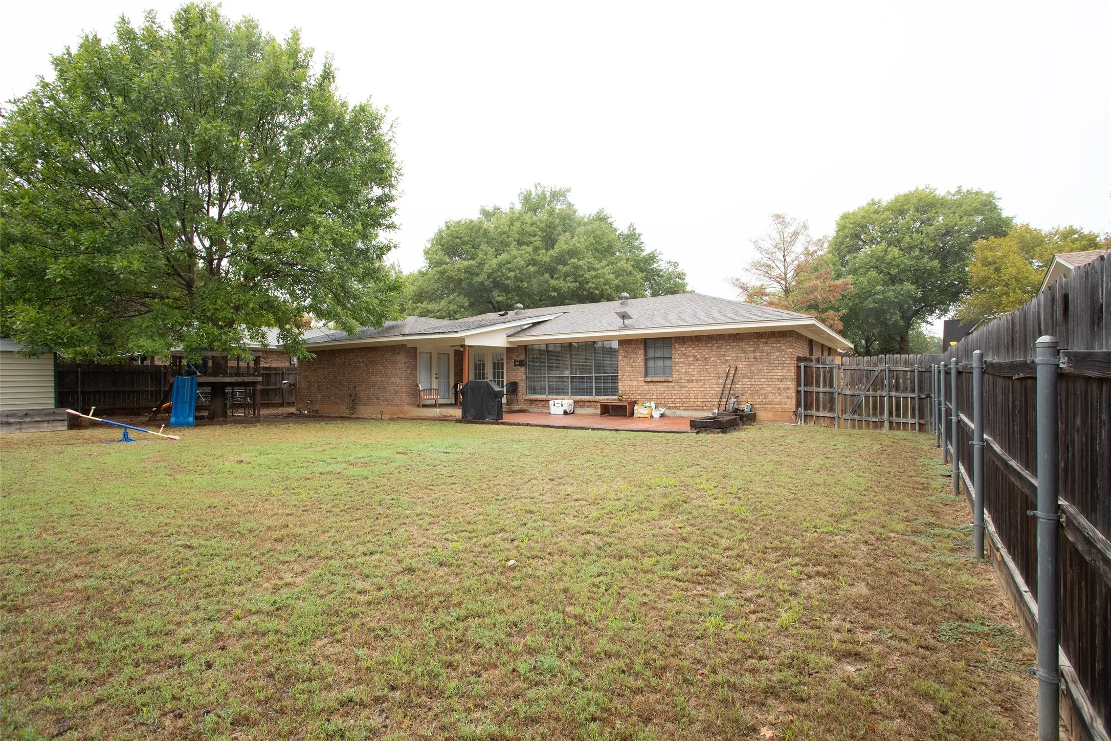 Expansive backyard with a large wooden deck, mature trees, and a full privacy fence