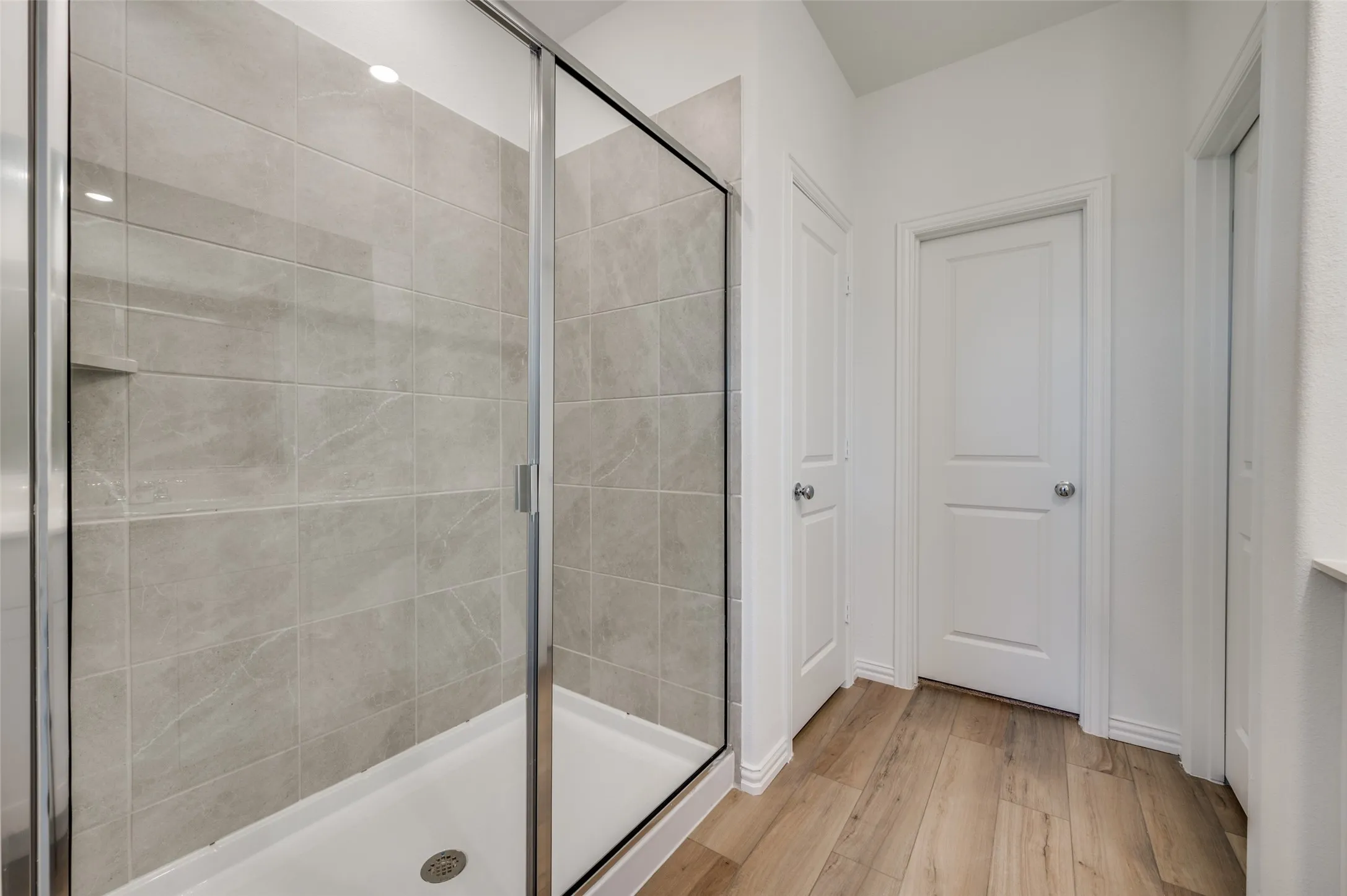 Glass-enclosed shower with a recessed shelf, light-toned tile surround, and wood-finish flooring