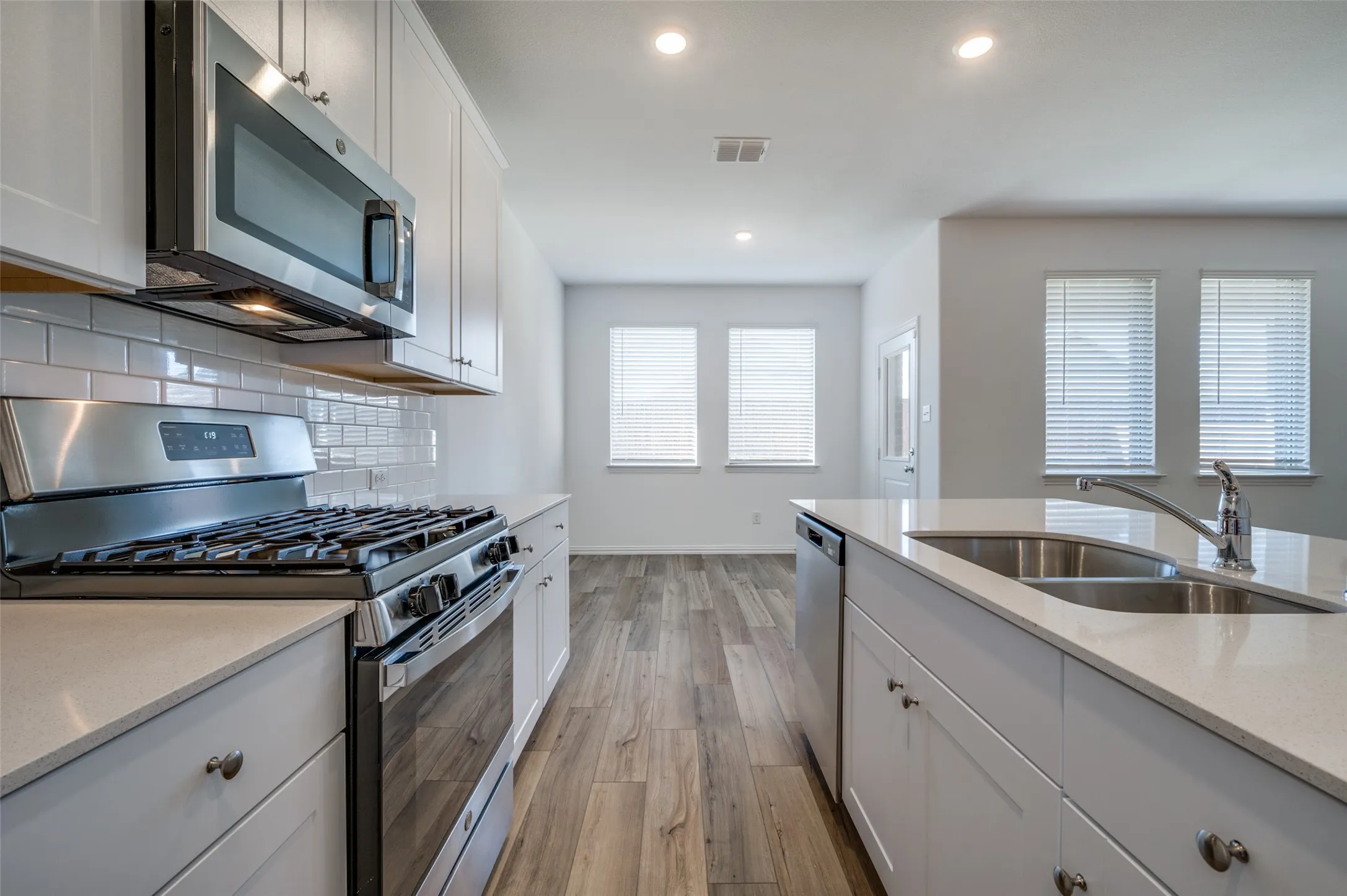 Kitchen featuring white shaker cabinetry, stainless steel appliances, light-toned countertops, subway tile backsplash, and wood-finish flooring