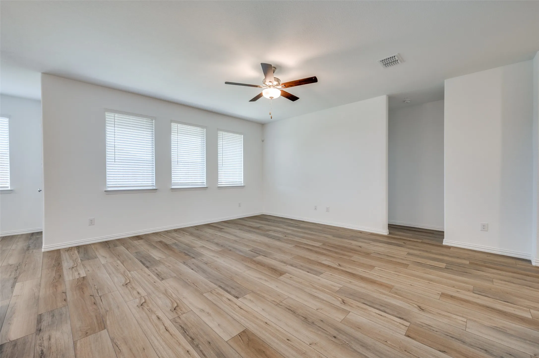 Expansive room featuring wood-finish flooring, multiple windows with blinds, and a ceiling fan