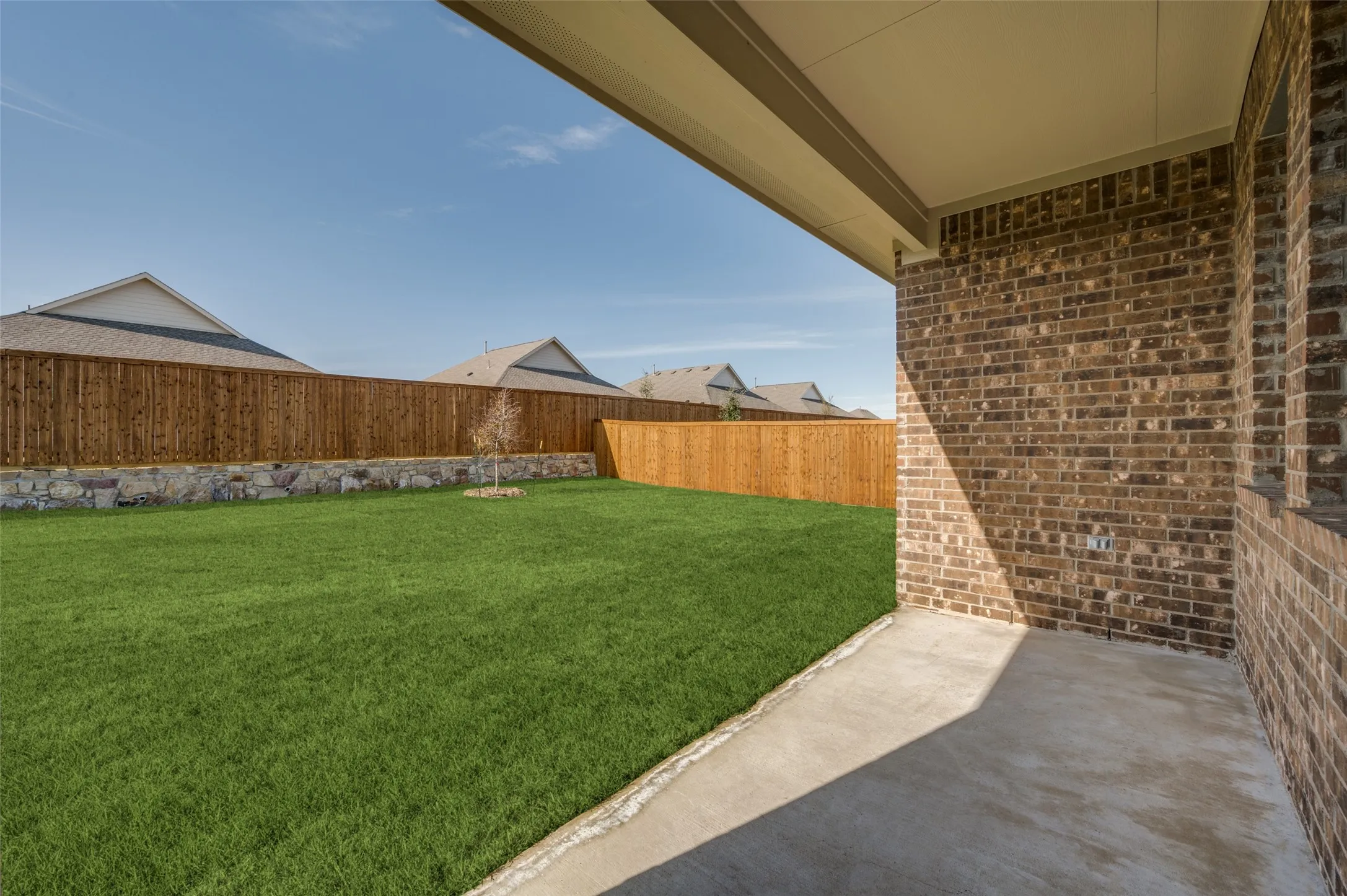 Covered patio with a concrete surface, a brick exterior wall, and a wood-paneled ceiling