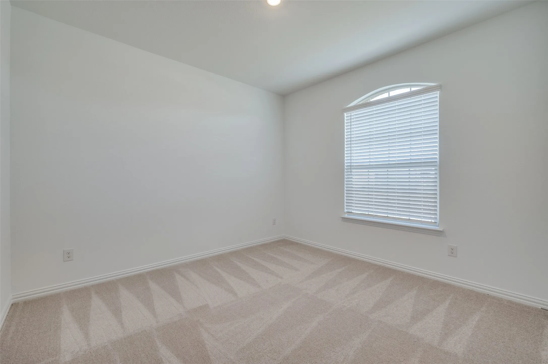 Recessed overhead lighting, an arched window with blinds, and neutral-toned carpeting