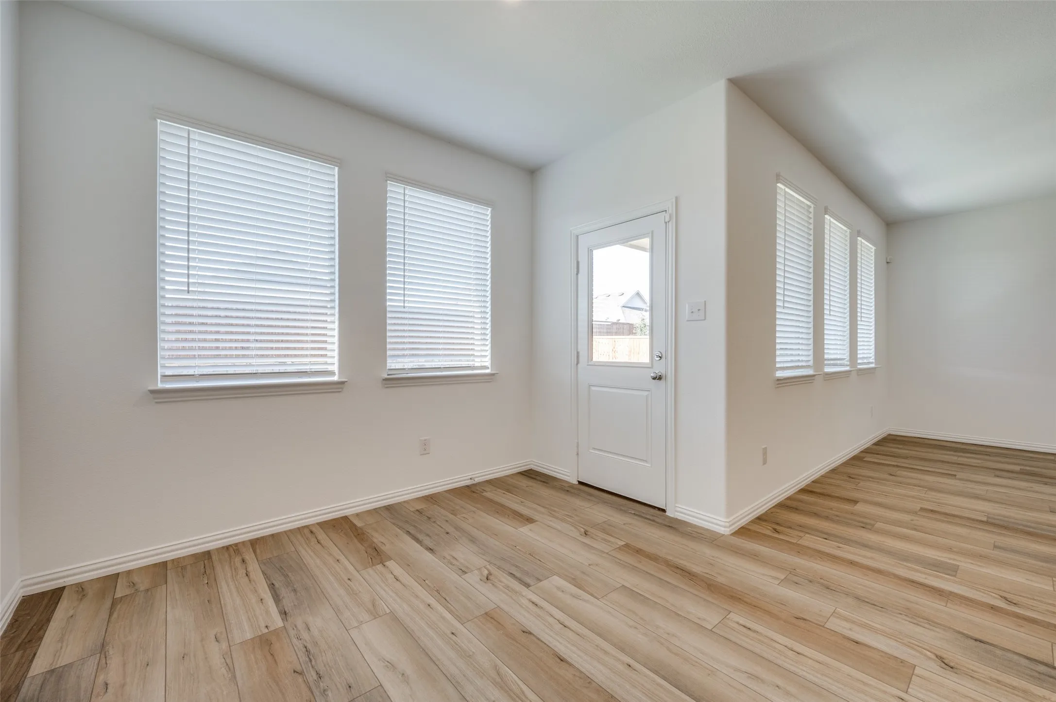 Wood-finish flooring throughout, multiple windows with blinds, white trim, and a full-light door