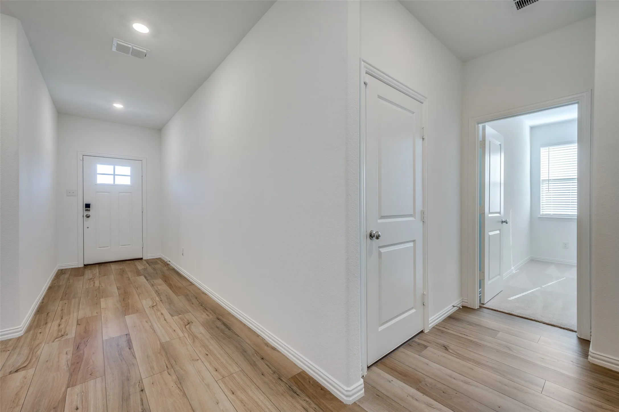 Wood-finish flooring throughout the hallway, white interior doors, and recessed lighting