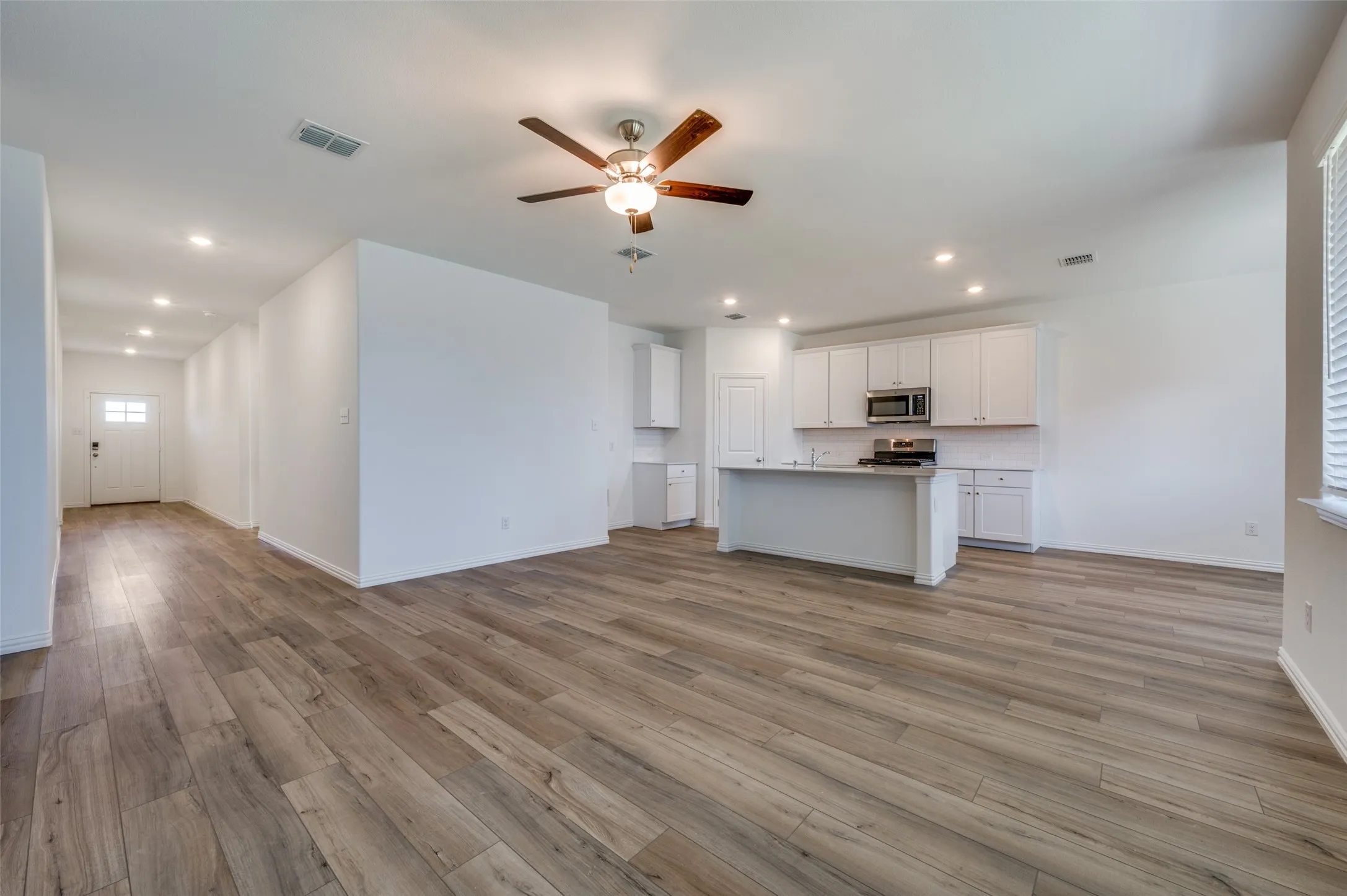 Open-concept floor plan featuring wood-finish flooring, recessed lighting, a modern ceiling fan, white cabinetry, and stainless steel appliances