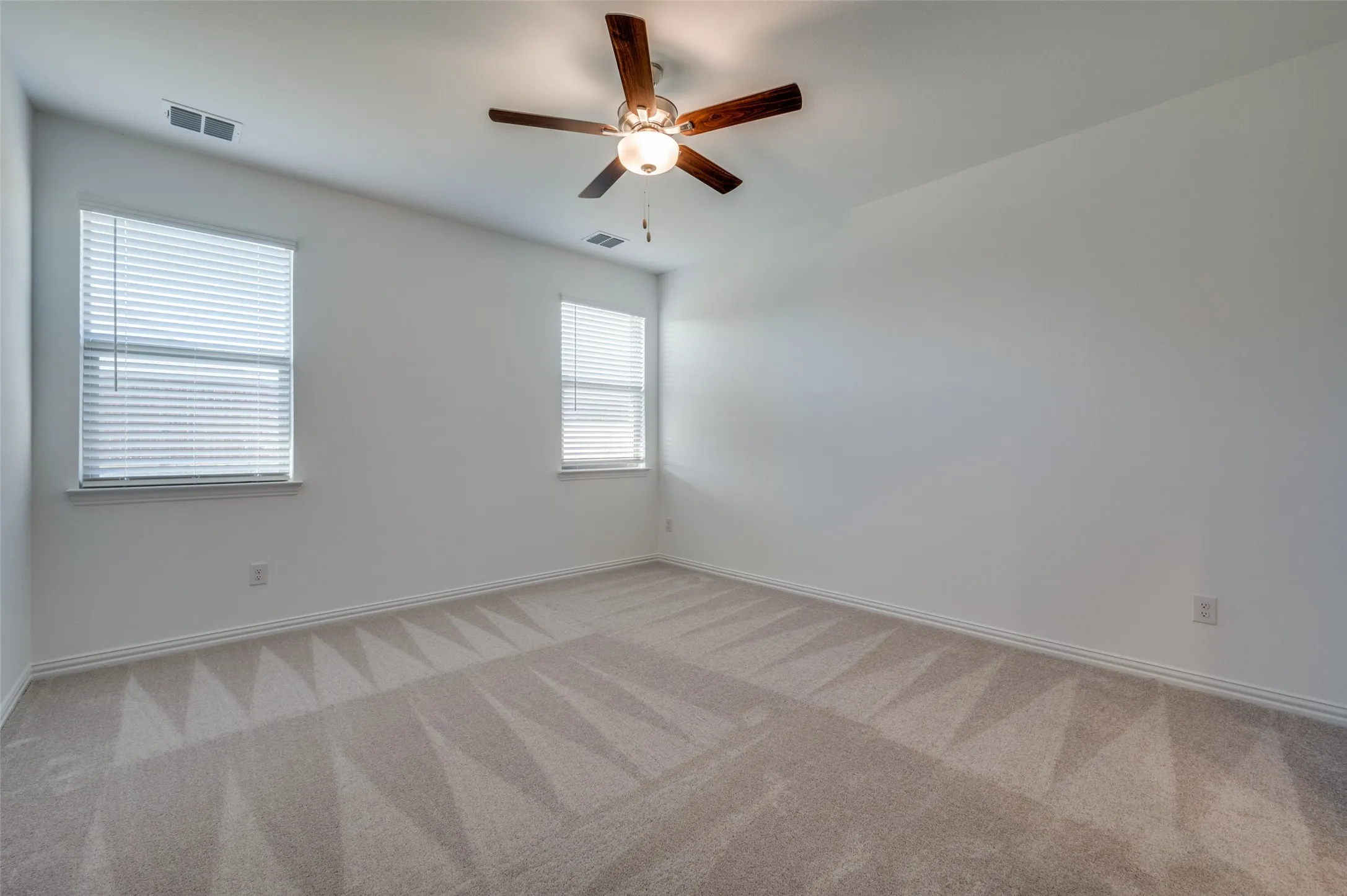 Neutral tone wall paint, light neutral carpet, two windows with blinds, and a ceiling fan with integrated lighting