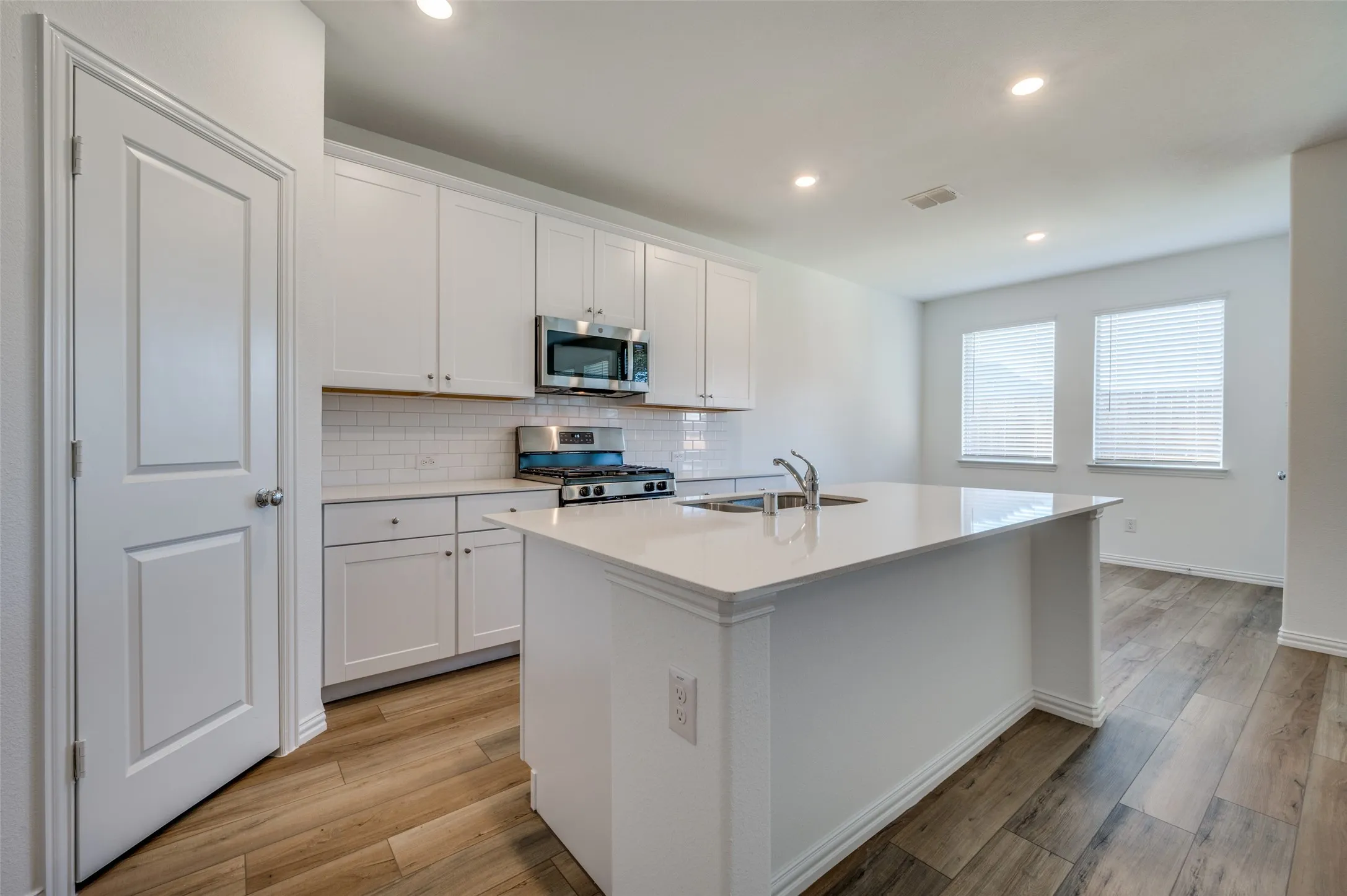 Kitchen featuring white cabinetry, stainless steel appliances, a white subway tile backsplash, a large center island with an integrated sink, and wood-finish flooring