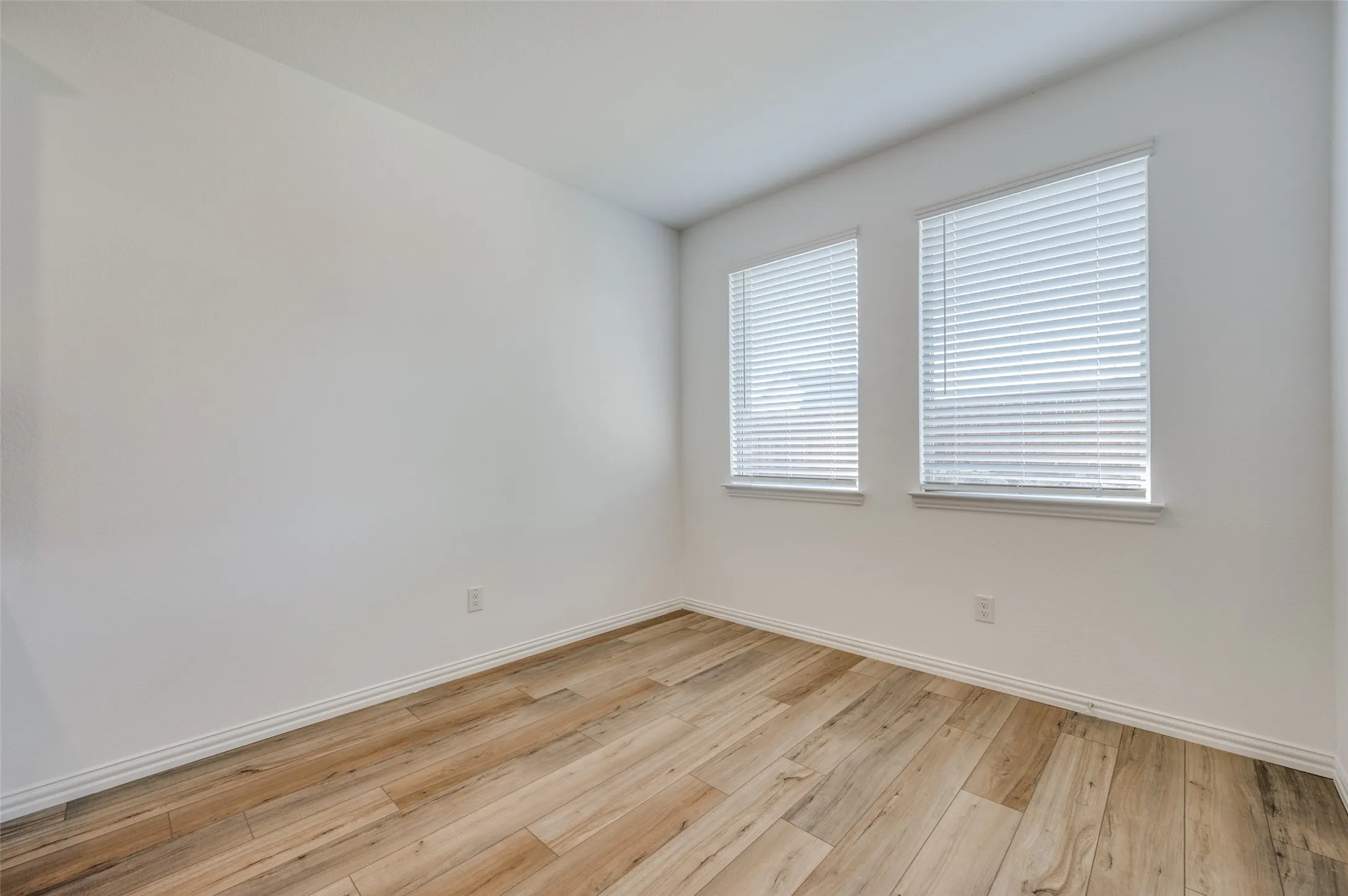 Wood-finish flooring, white walls, and two windows with blinds