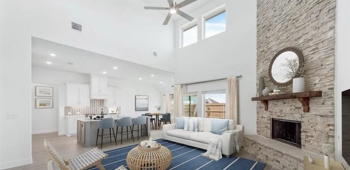 Living room featuring a towering ceiling, a fireplace, ceiling fan, healthy amount of natural light, and light wood-type flooring